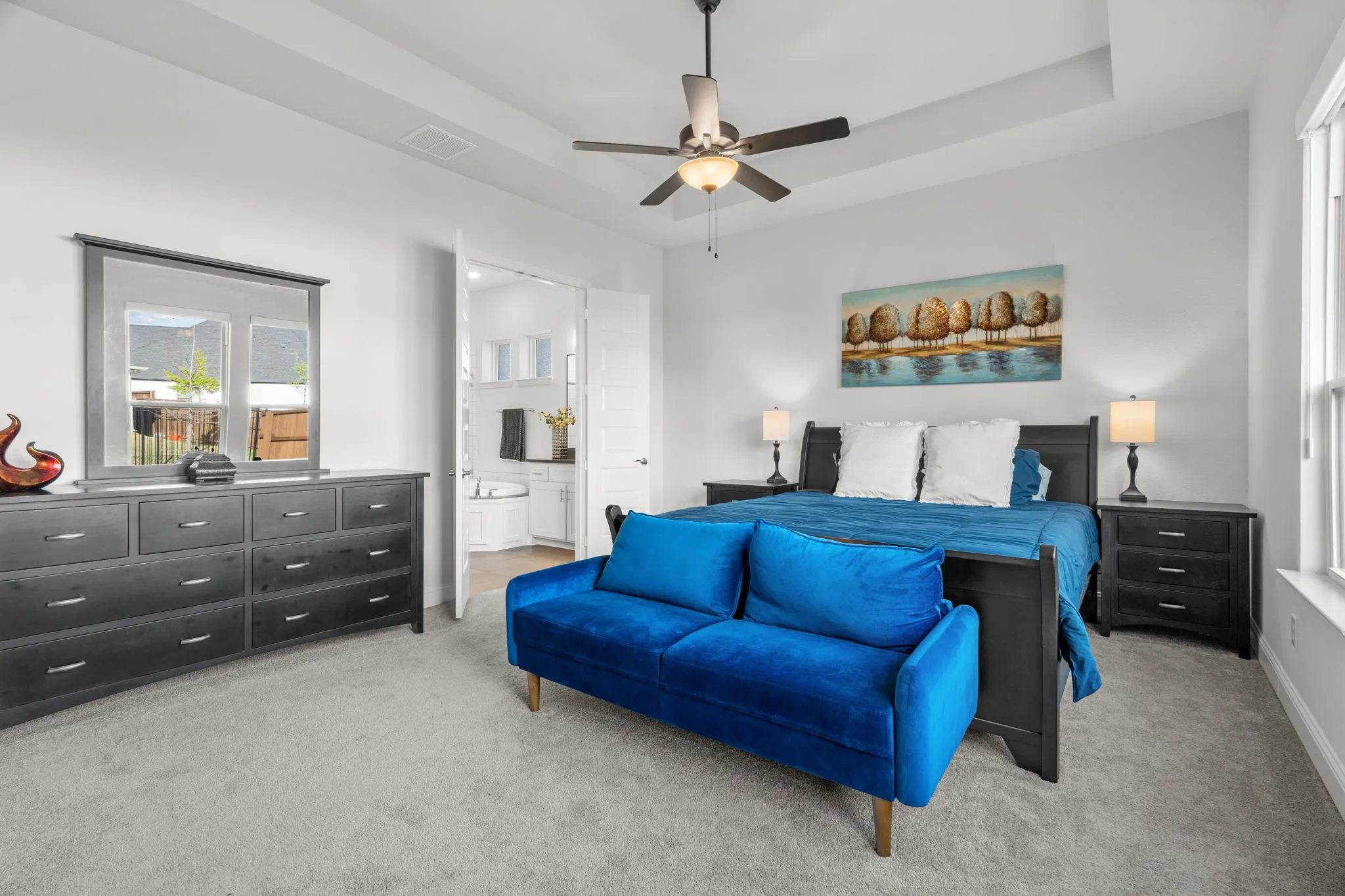 Spacious bedroom featuring light grey carpeting, white walls, a ceiling fan with integrated lighting, and a tray ceiling