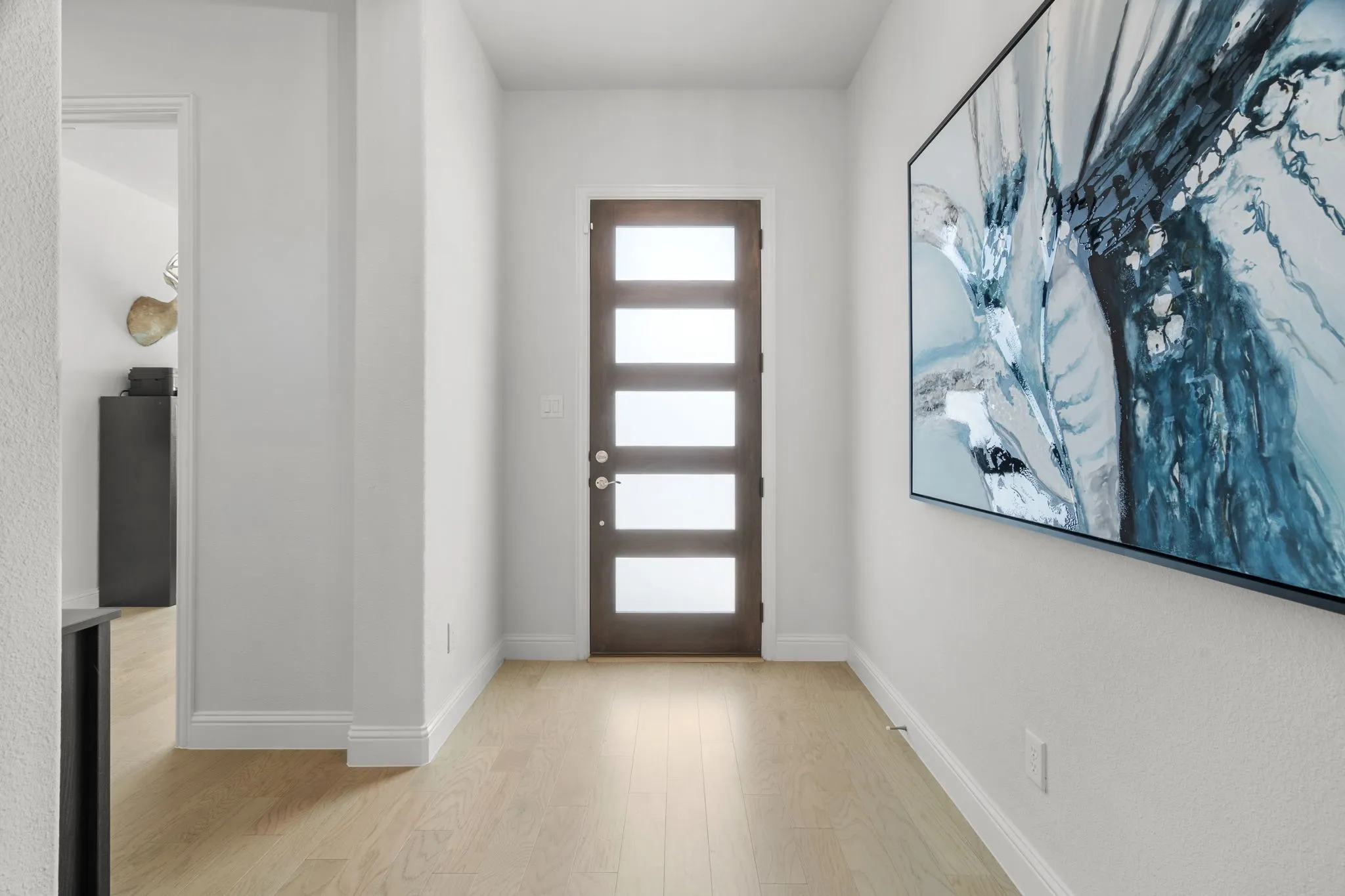 Entryway featuring a dark wood door with five frosted glass panels, light wood-finish flooring, and crisp white walls