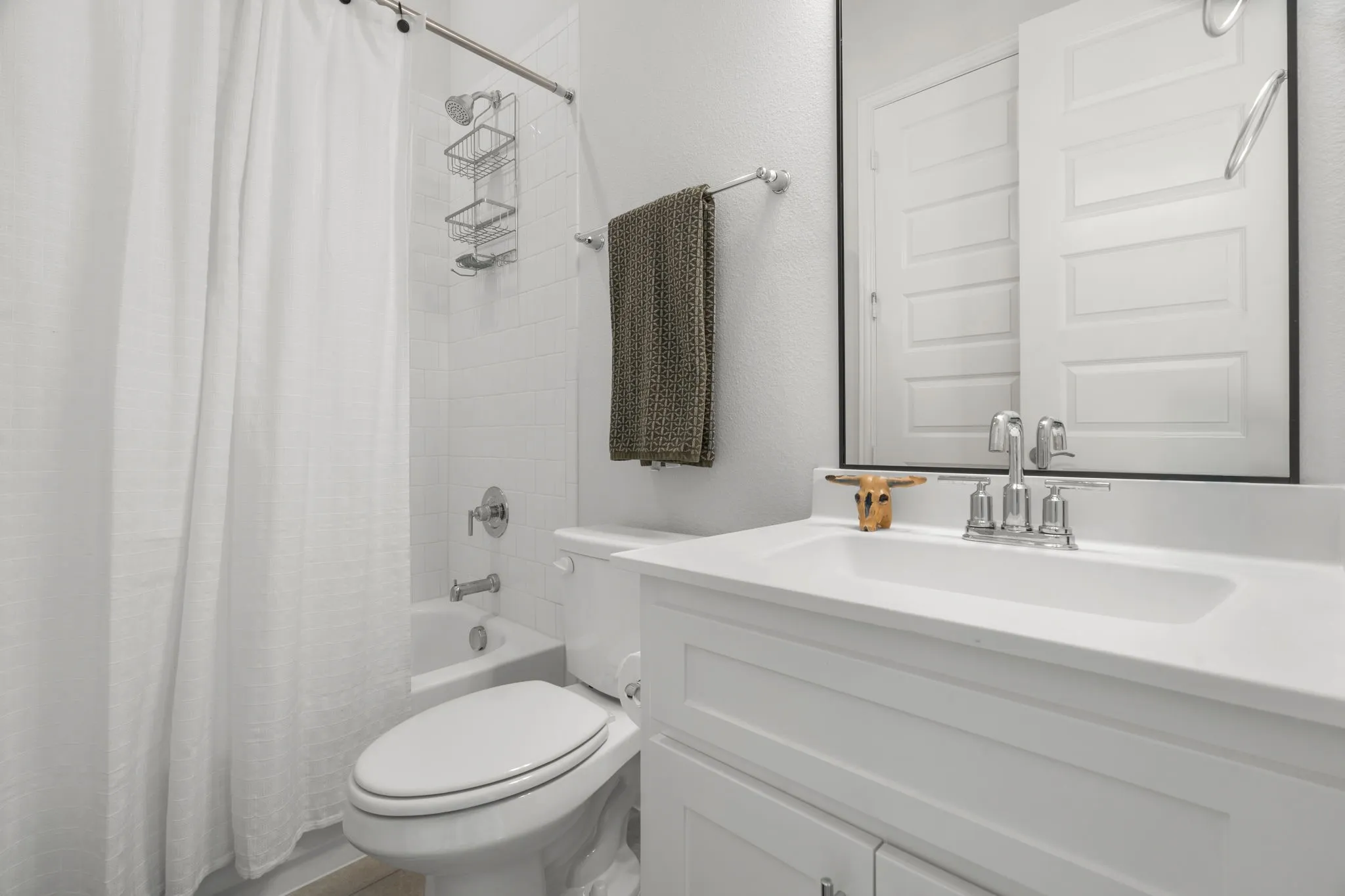 Bathroom featuring a white vanity with an integrated sink, a rectangular framed mirror, a full-size bathtub with a shower, white subway tile surround, and chrome fixtures