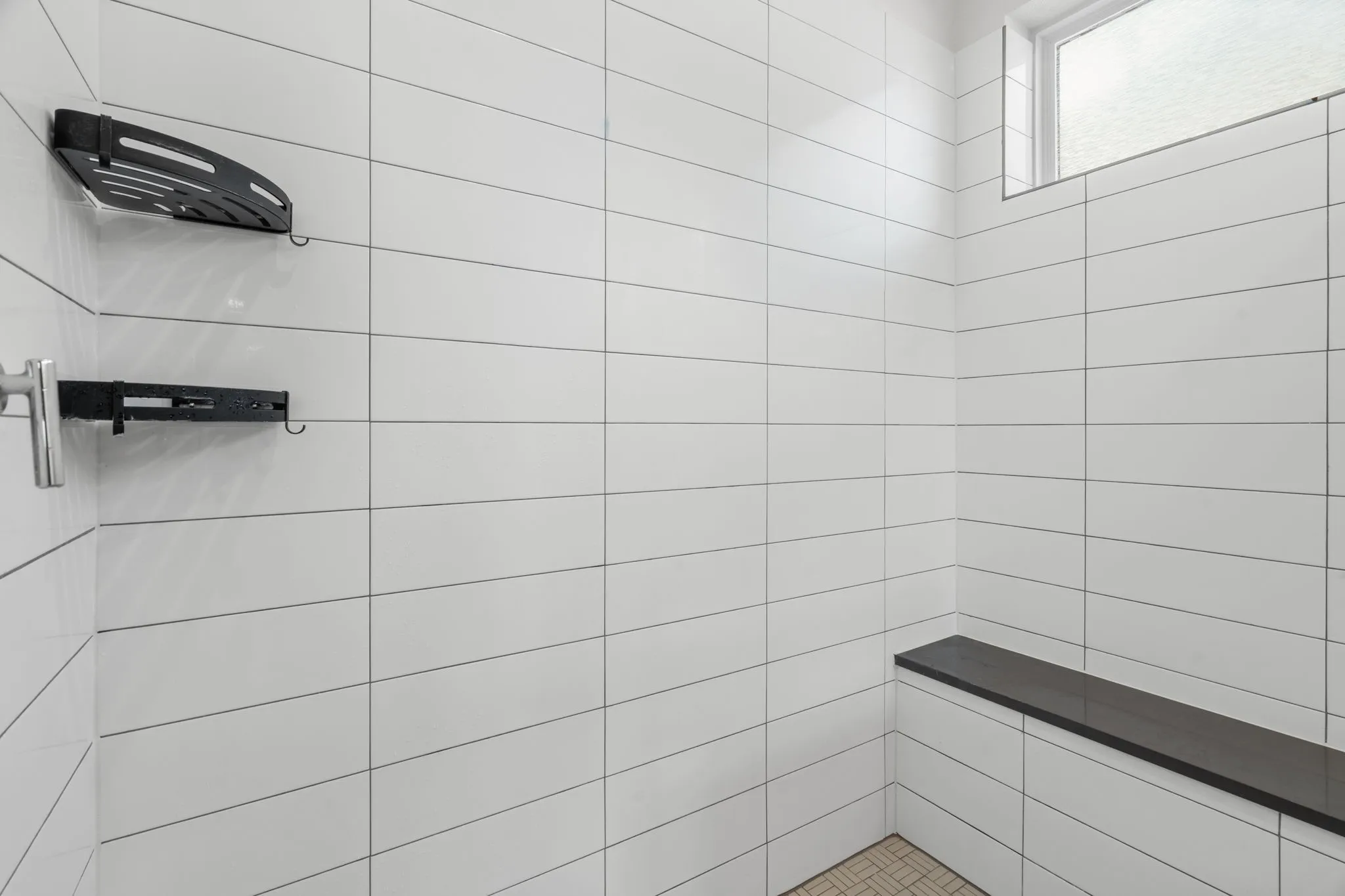 Tiled shower enclosure featuring white subway tile, a built-in dark bench, and a high-set window