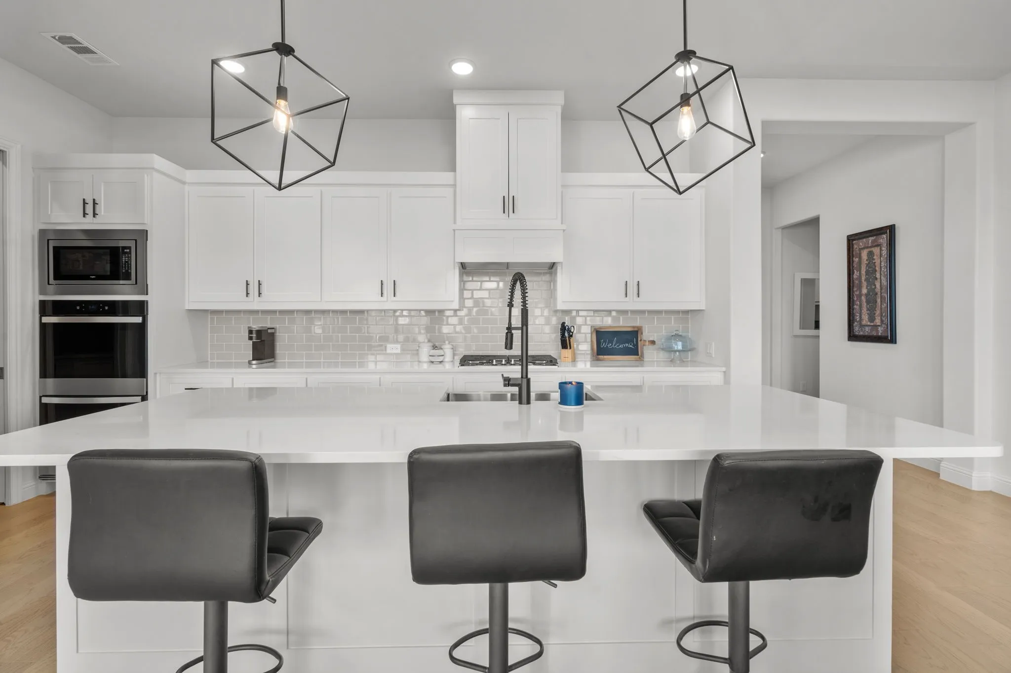 Contemporary kitchen featuring a large center island with seating, white shaker cabinetry, stainless steel double oven, built-in microwave, and geometric pendant lighting