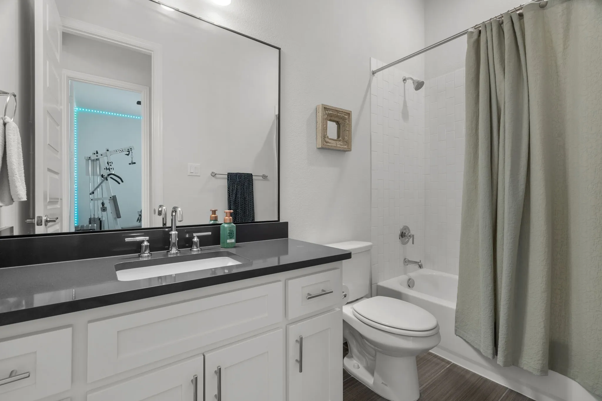 Bathroom featuring a single vanity with dark countertop, white shaker-style cabinetry, and a rectangular undermount sink