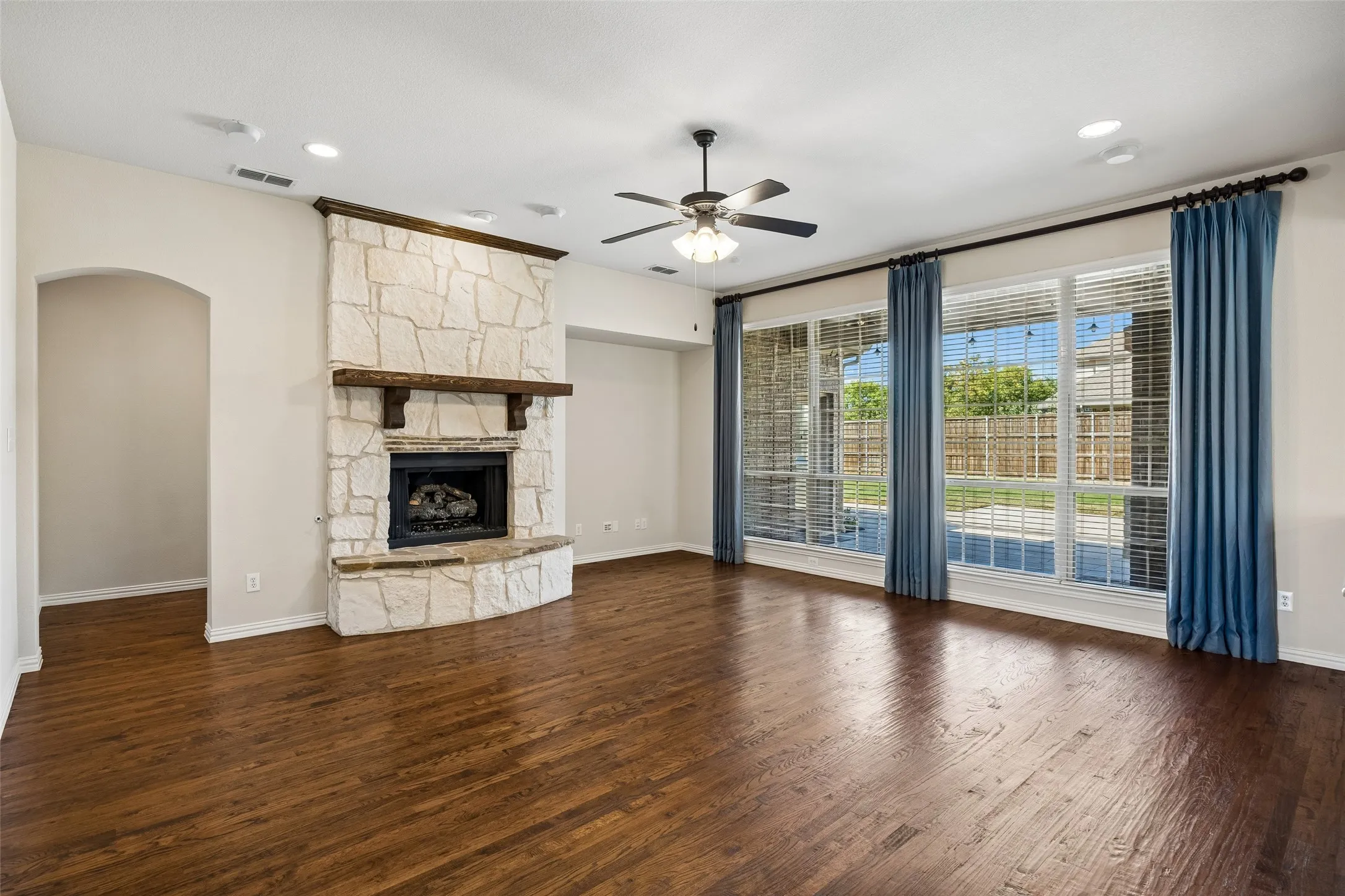 Spacious living area featuring wood-finish flooring, a stone fireplace with a wood mantle, and multiple large windows