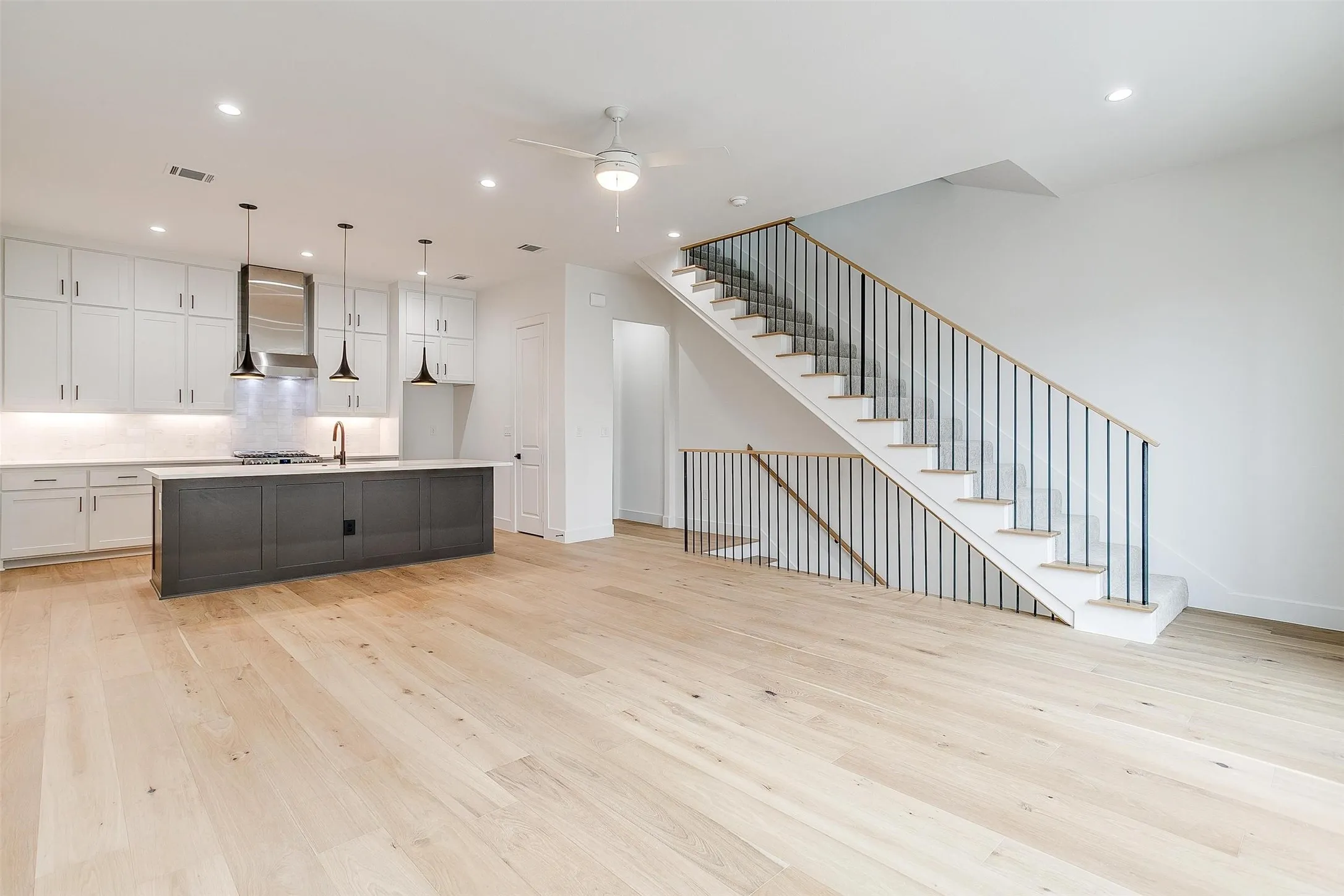 Kitchen with white cabinetry, light wood-type flooring, an island with sink, open floor plan, and backsplash