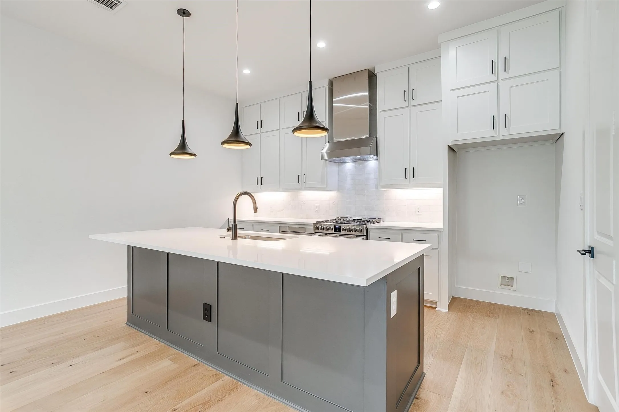 Kitchen featuring white cabinetry, tasteful backsplash, hanging light fixtures, an island with sink, and light wood finished floors