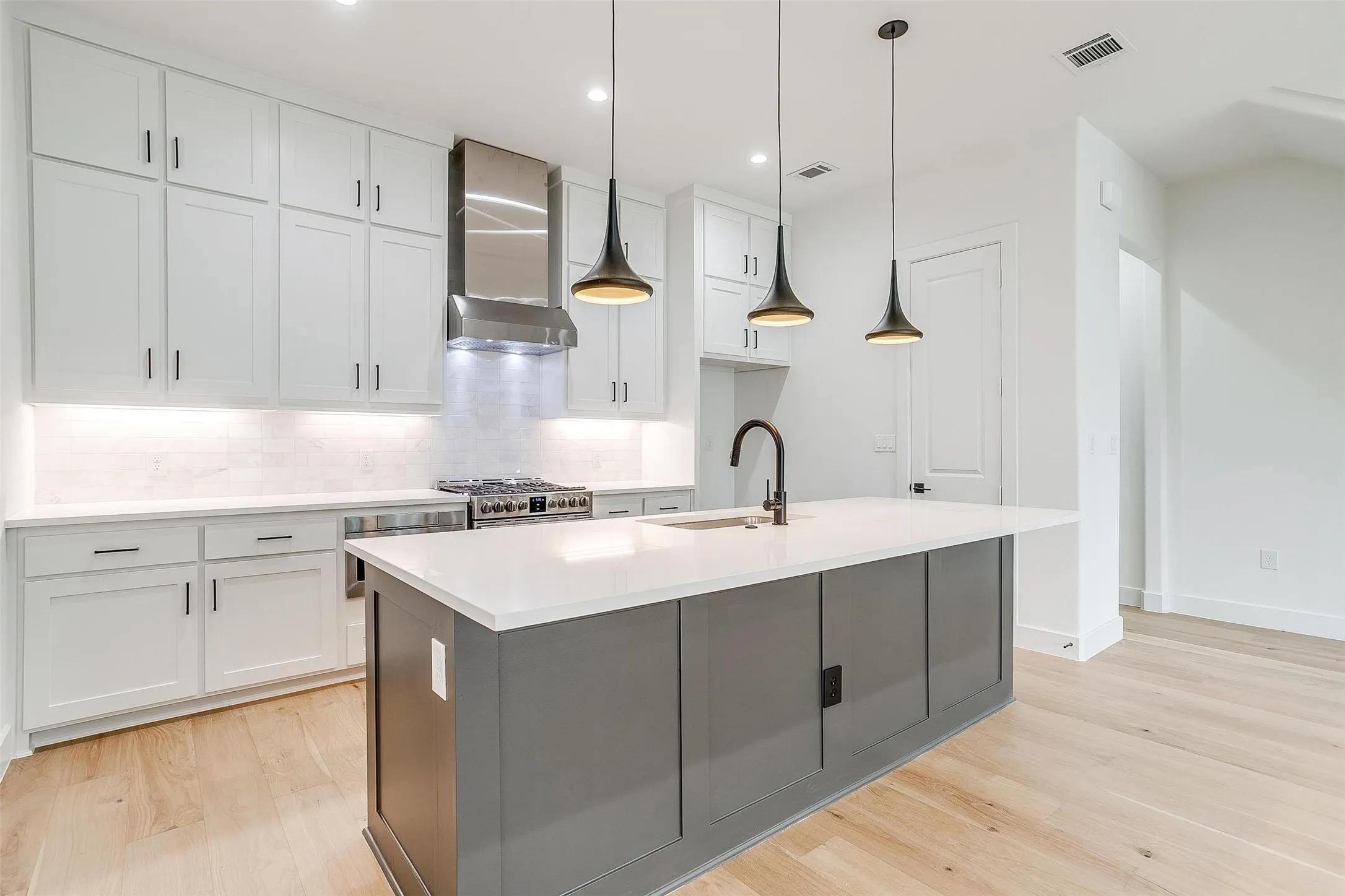 Kitchen with decorative backsplash, light wood-style flooring, a center island with sink, decorative light fixtures, and wall chimney range hood
