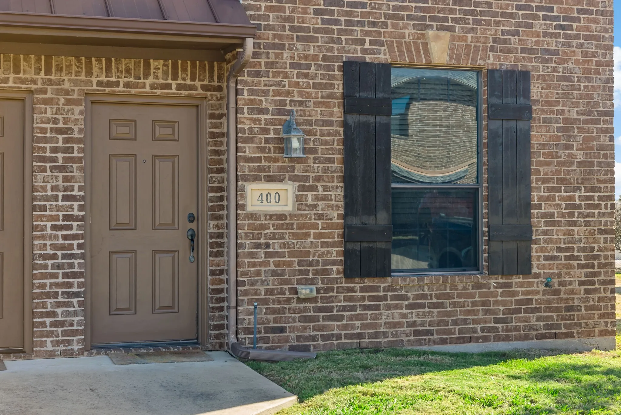 Brick exterior with a paneled entry door, address plaque, and a window with dark wood shutters