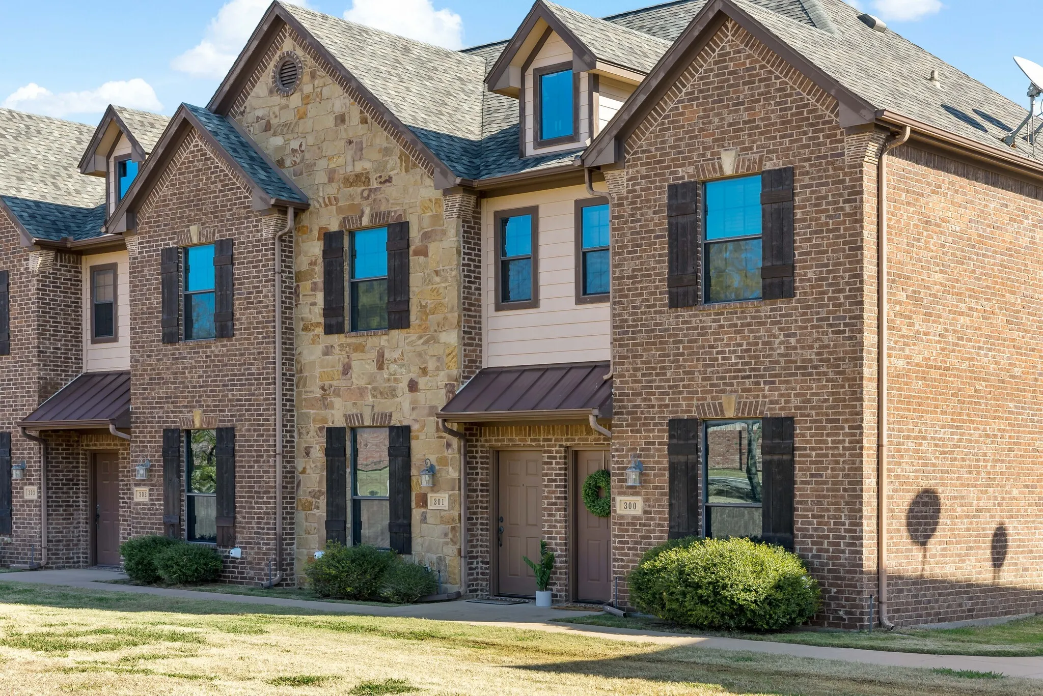 Brown brick and natural stone veneer exterior featuring dark brown shutters and coordinating metal awnings
