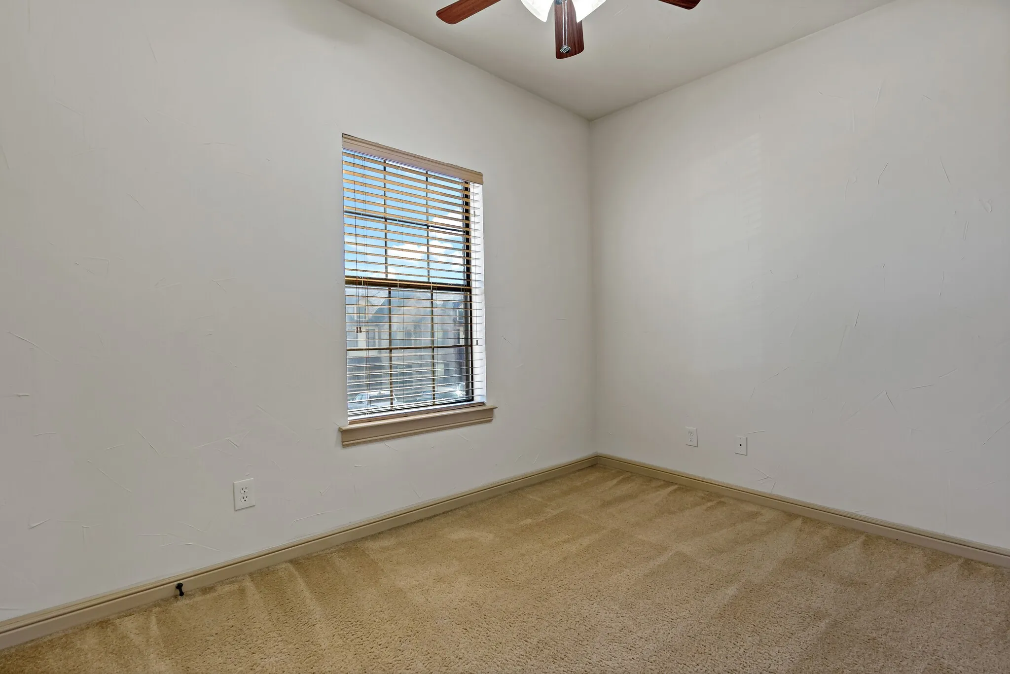 Interior room featuring neutral-toned carpet, a ceiling fan with wood-finish blades, and a window with blinds