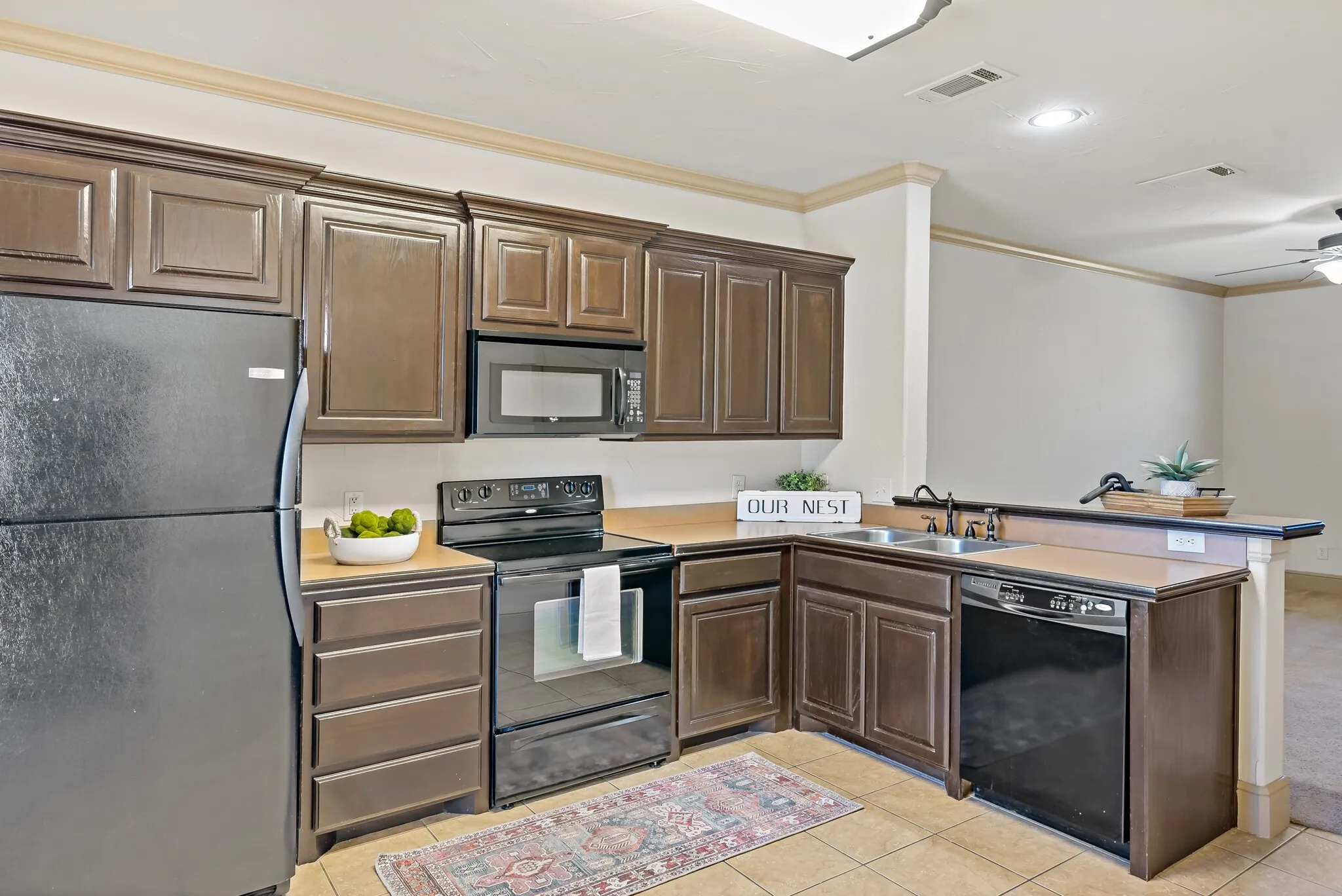 Kitchen featuring dark wood cabinetry, black appliances, a double basin sink, and tile flooring