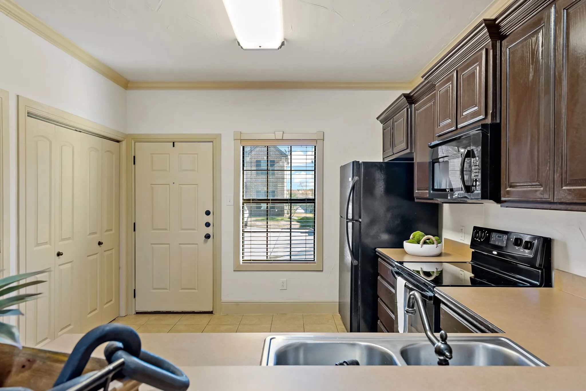 Kitchen featuring dark wood cabinetry, black appliances, a double basin stainless steel sink, and light-toned countertops