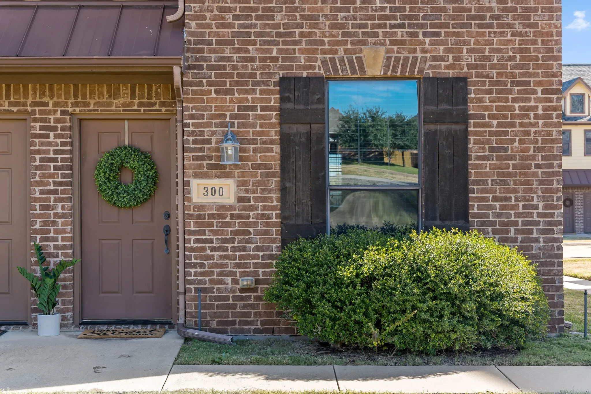 Brick facade featuring a panel door, decorative window shutters, and a prominent house number plaque