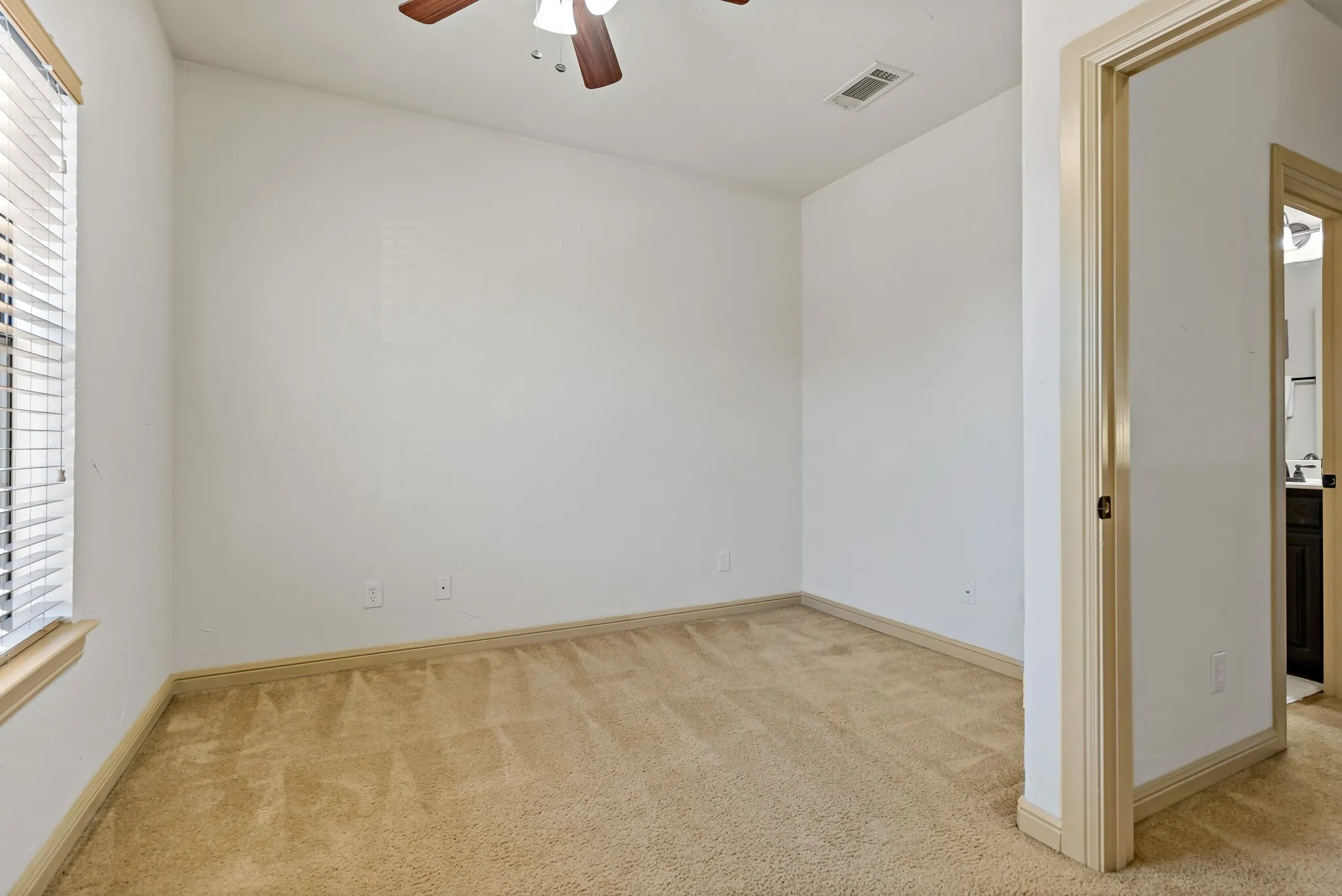 Carpeted interior space featuring a window with horizontal blinds, a ceiling fan with integrated lighting, and a recessed ceiling vent