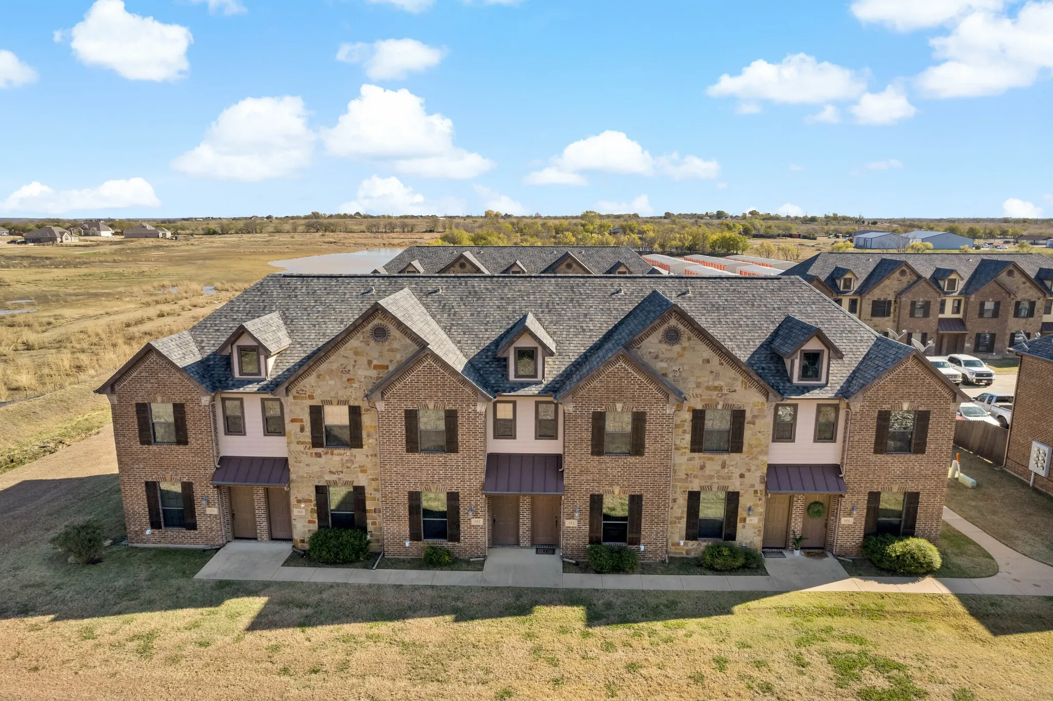 Townhome exterior featuring a combination of brick and stone facade, dormer windows, dark asphalt shingle roofing, and dark shutters