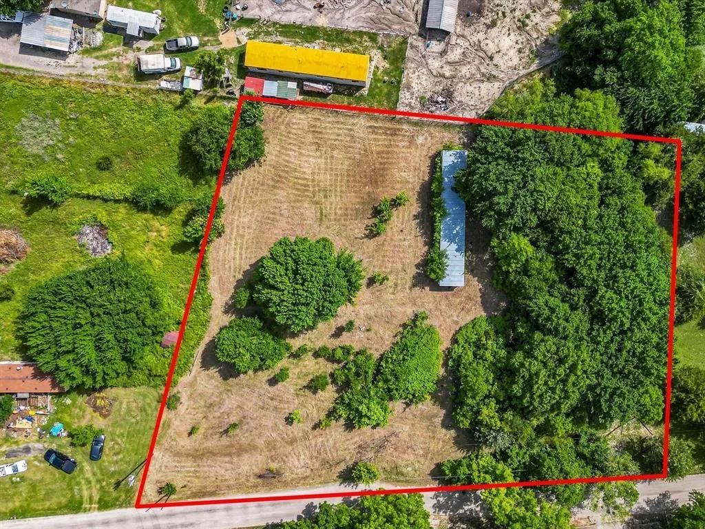 Expansive parcel featuring a mix of cleared land and mature trees, with a structure featuring a metal roof