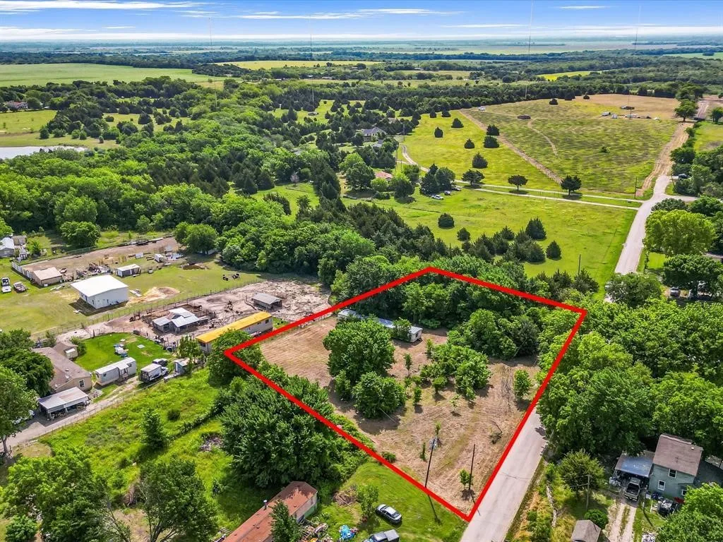 Expansive land parcel featuring a mix of mature trees and open ground, bordered by a paved road