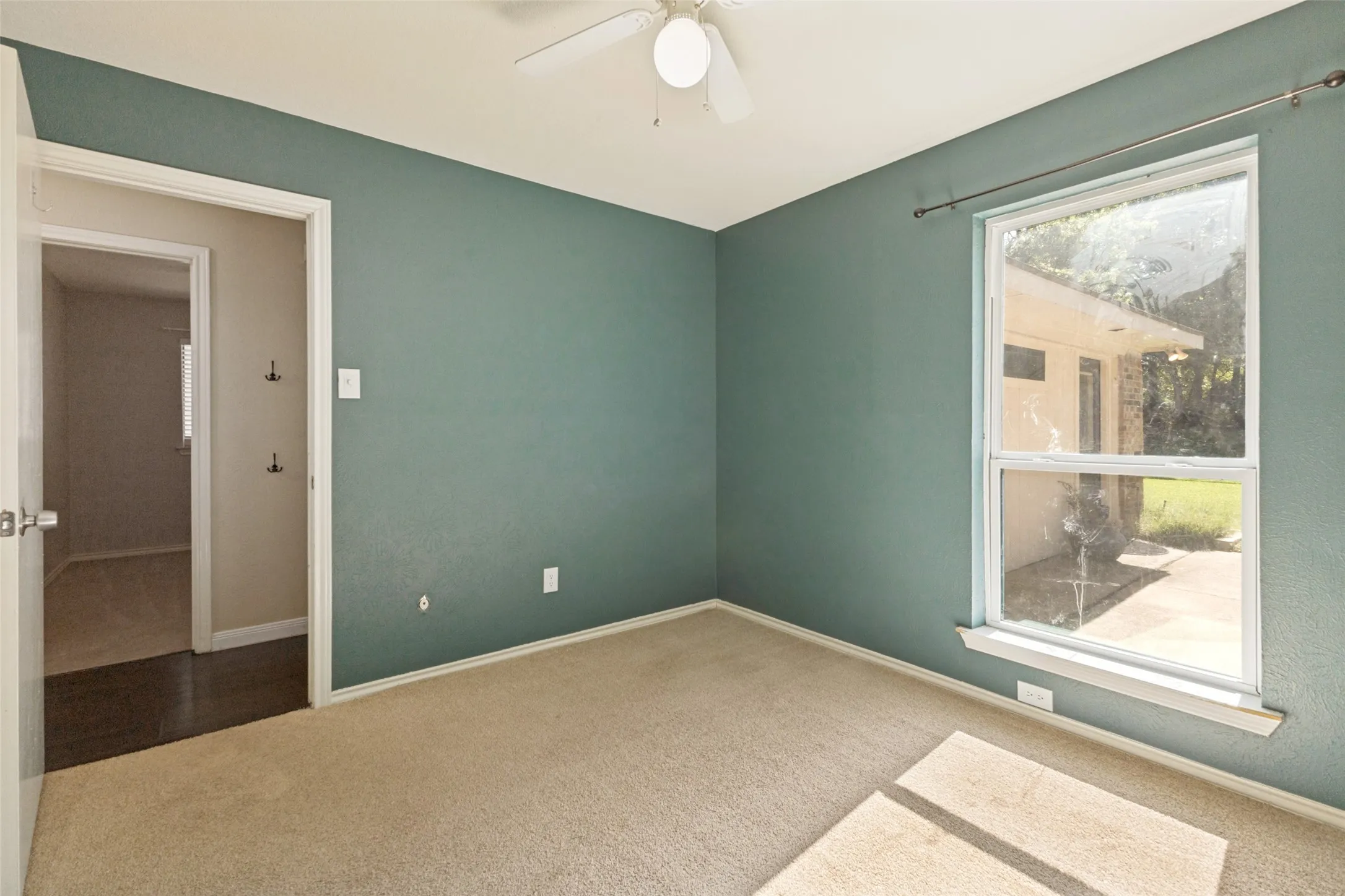Carpeted room with a ceiling fan, a window, and a white door frame