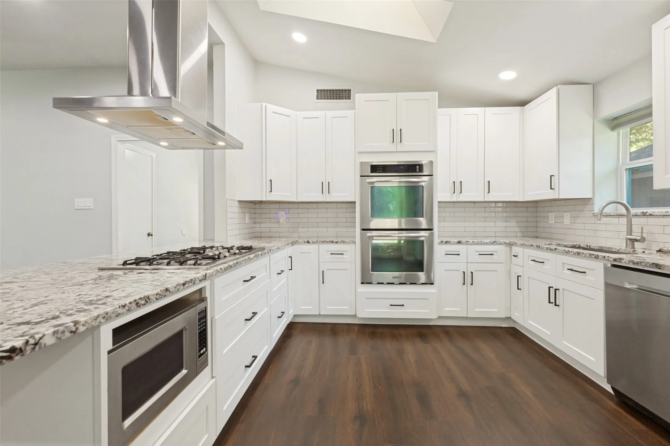 Modern kitchen featuring white shaker cabinetry, stainless steel appliances, speckled stone countertops, a subway tile backsplash, and dark wood-finish flooring