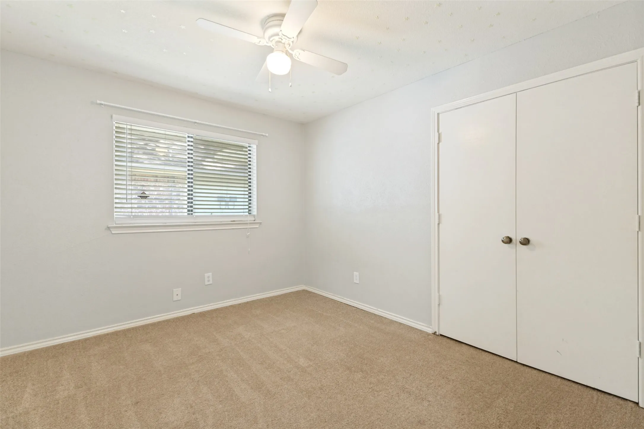 Carpeted room with a ceiling fan, a window featuring horizontal blinds, and a built-in closet with bi-fold doors