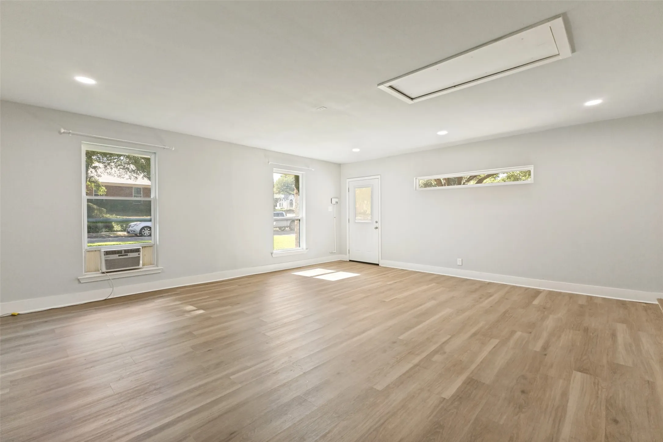 Spacious room featuring wood-finish flooring, recessed lighting, and a white entry door