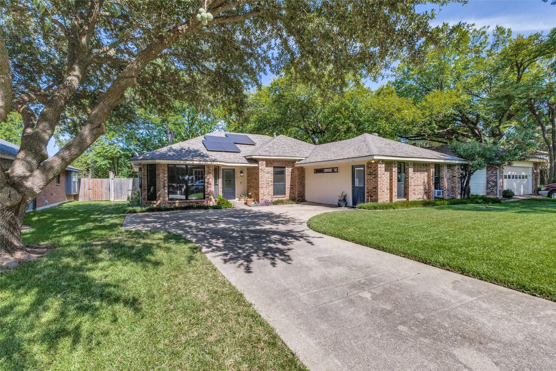 Brick veneer exterior with a concrete driveway, mature trees, and solar panels