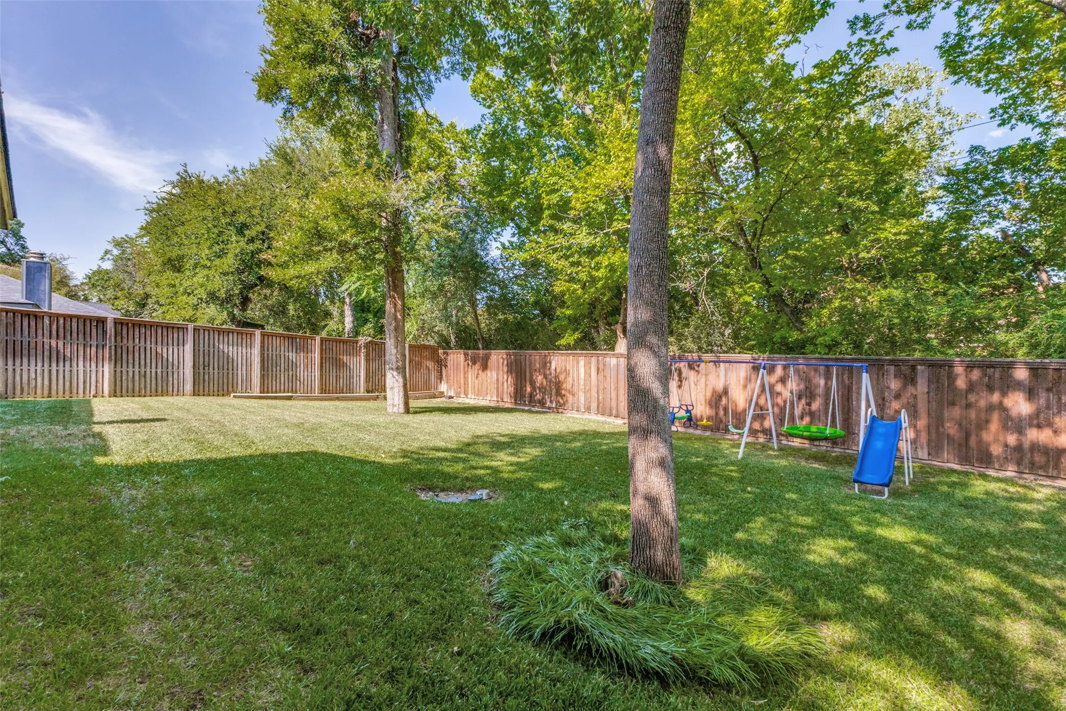 Expansive backyard featuring a manicured lawn, established trees, and perimeter wood fencing
