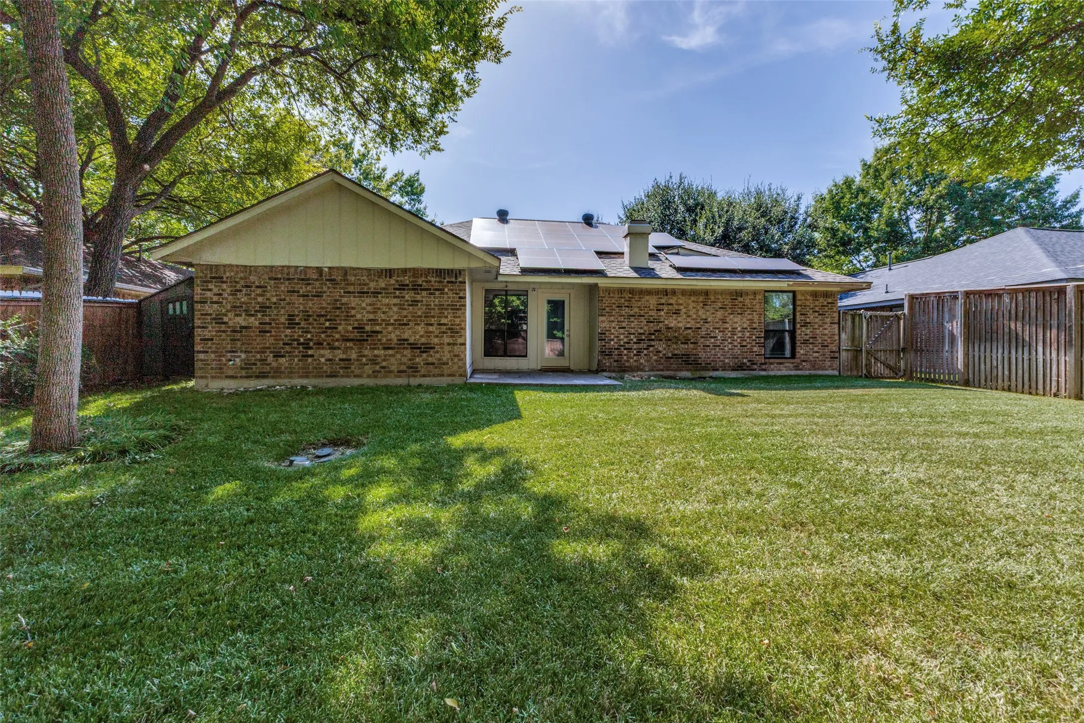 Expansive backyard featuring a lush lawn, mature trees, and a brick exterior with solar panels