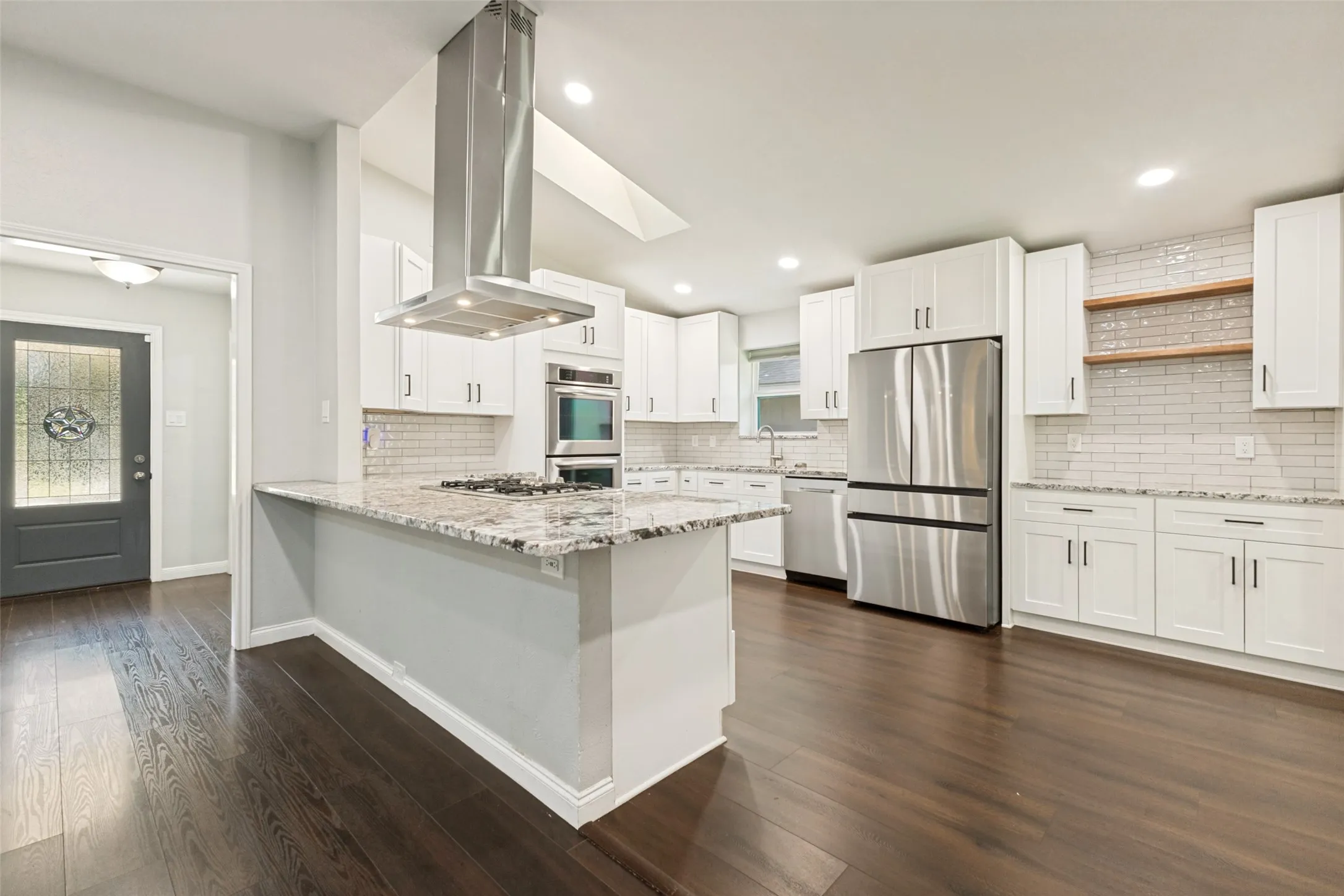 Modern kitchen featuring a large island with a gas cooktop, stainless steel appliances, white shaker cabinetry, white subway tile backsplash, and dark wood-finish flooring