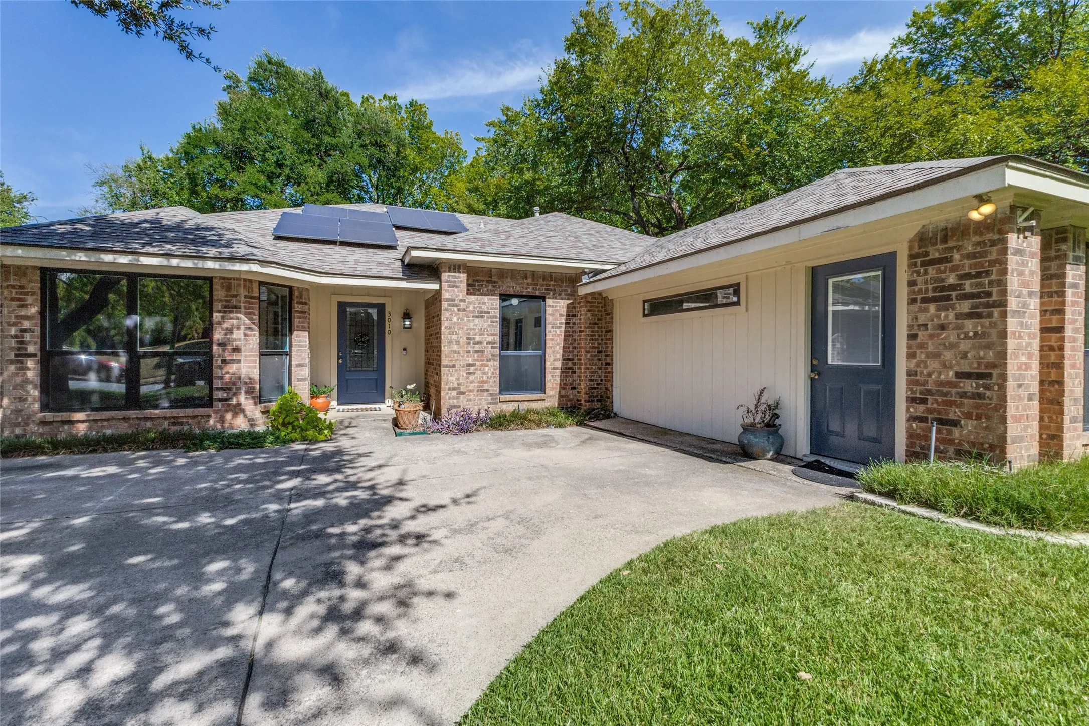 Brick facade residence featuring a multi-panel solar array, a dark-toned front entry door, and a concrete driveway
