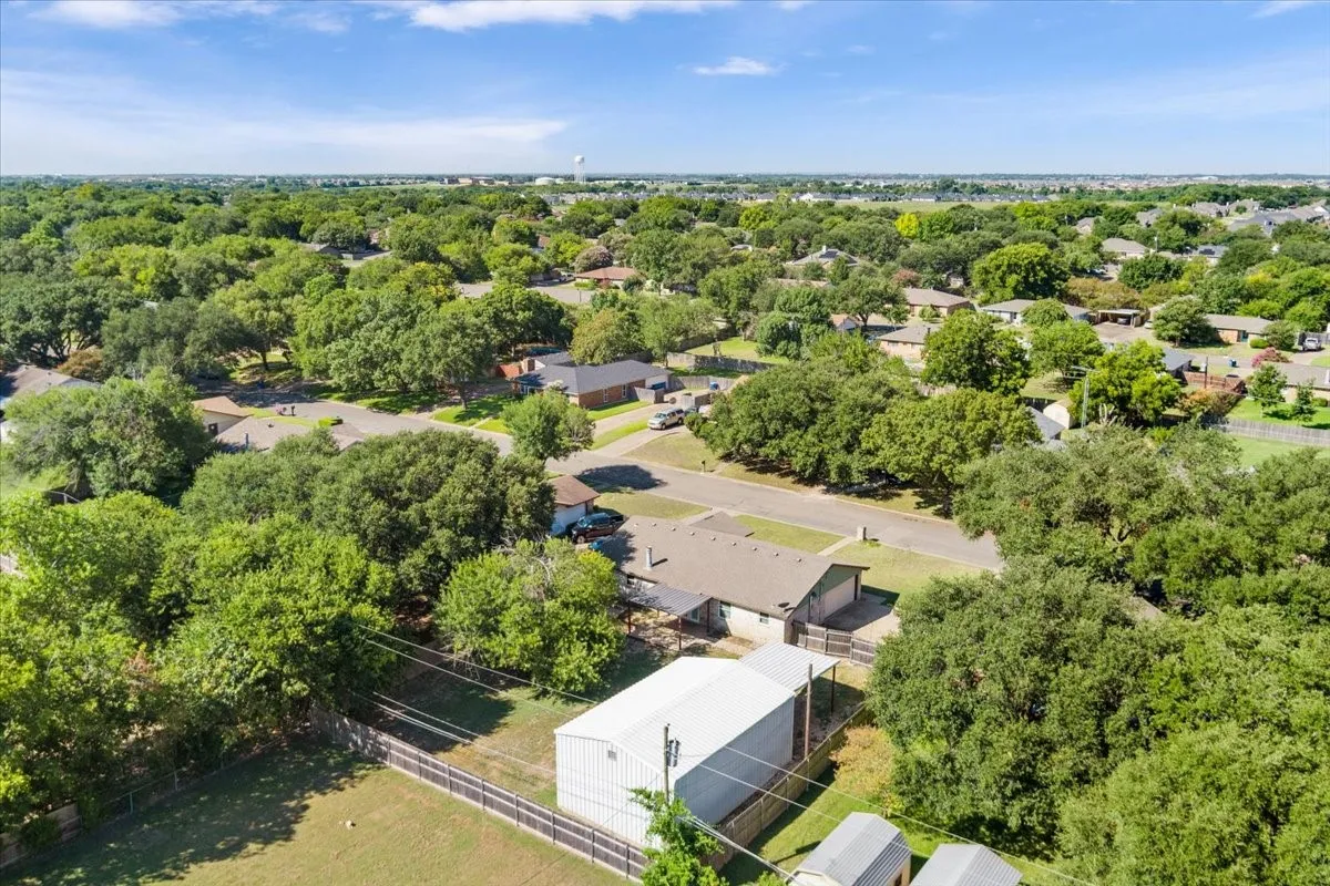 Aerial perspective of a residential area featuring numerous mature trees and a clear sky