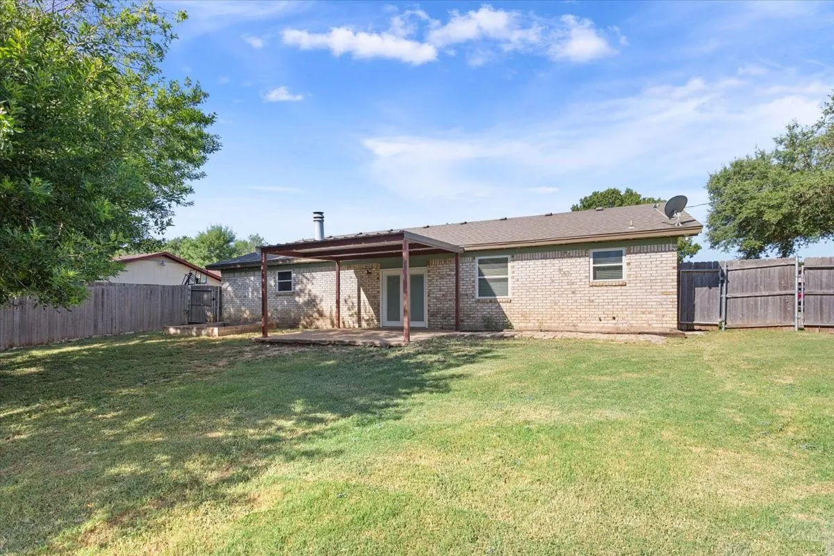 Spacious backyard featuring a covered patio, brick exterior, full wood fencing, and a shingle roof