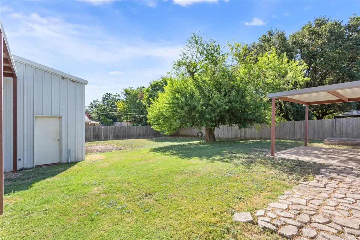 Expansive backyard featuring a large tree, a covered patio area, and a stone walkway