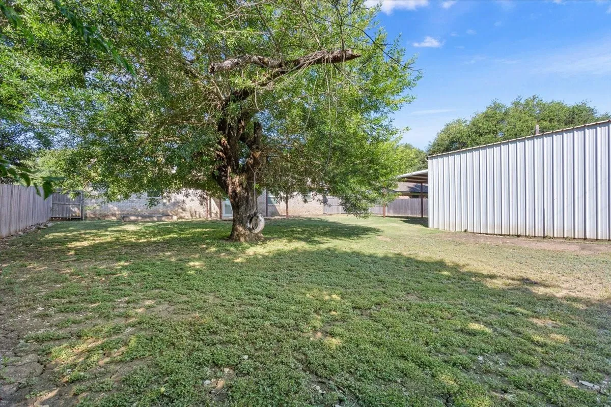 Spacious backyard featuring a mature shade tree, natural grass, and a metal-sided outbuilding