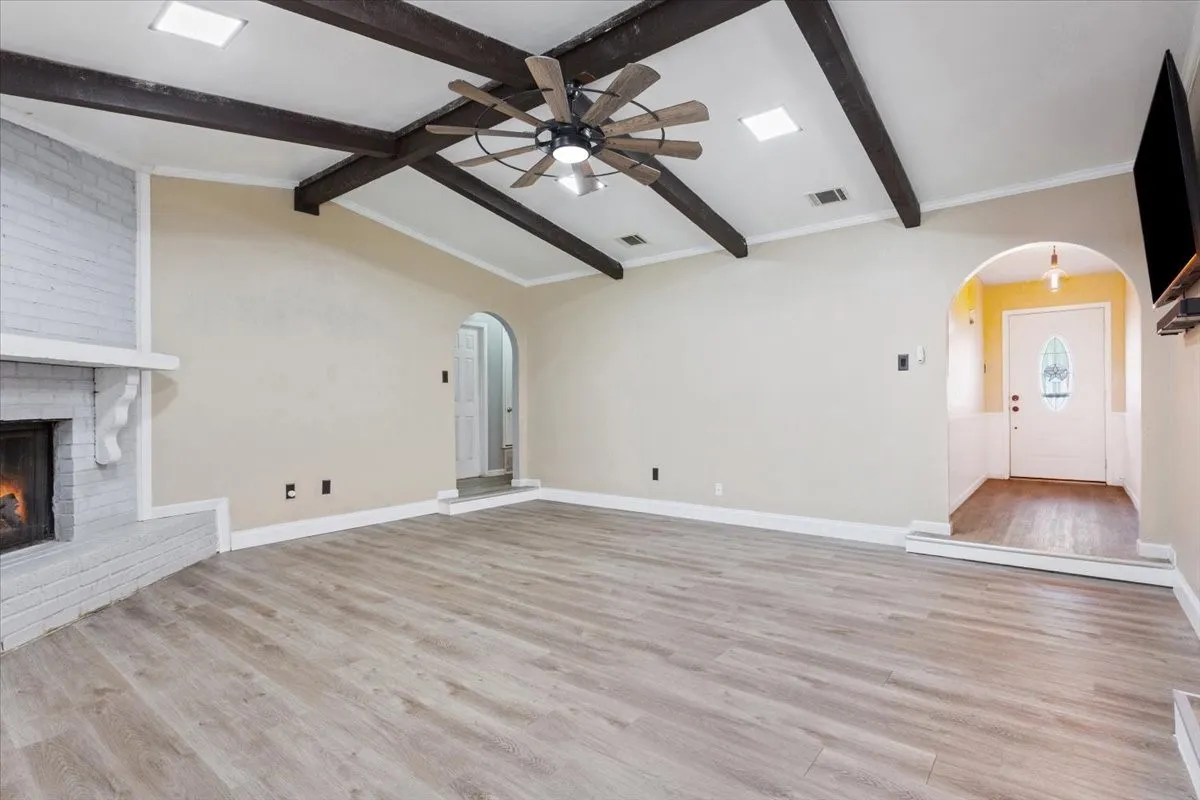 Spacious living area featuring light wood-finish flooring and a vaulted ceiling with exposed dark wood beams