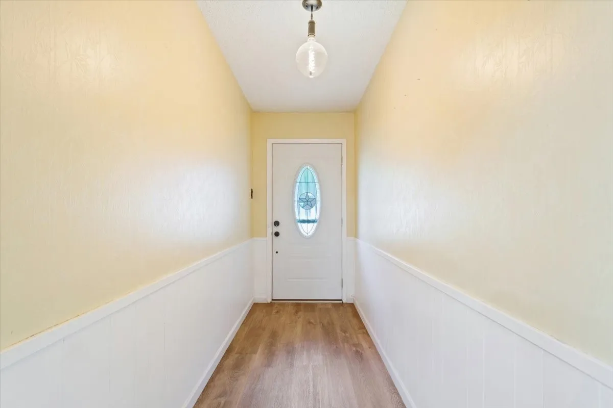 Entryway featuring a white door with decorative glass, wood-finish flooring, and wainscoting