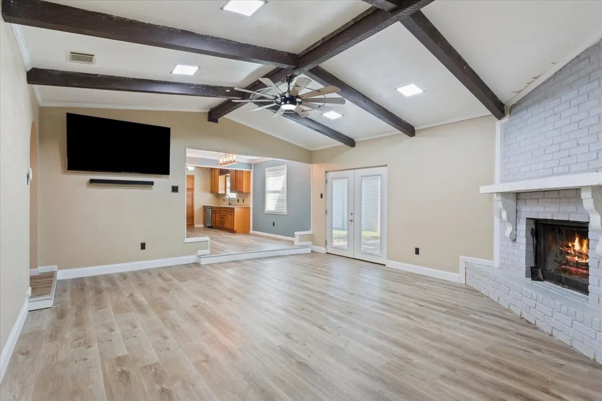 Vaulted ceiling with exposed wood beams, brick fireplace with a white mantel, wood-finish flooring, and double glass-paneled doors