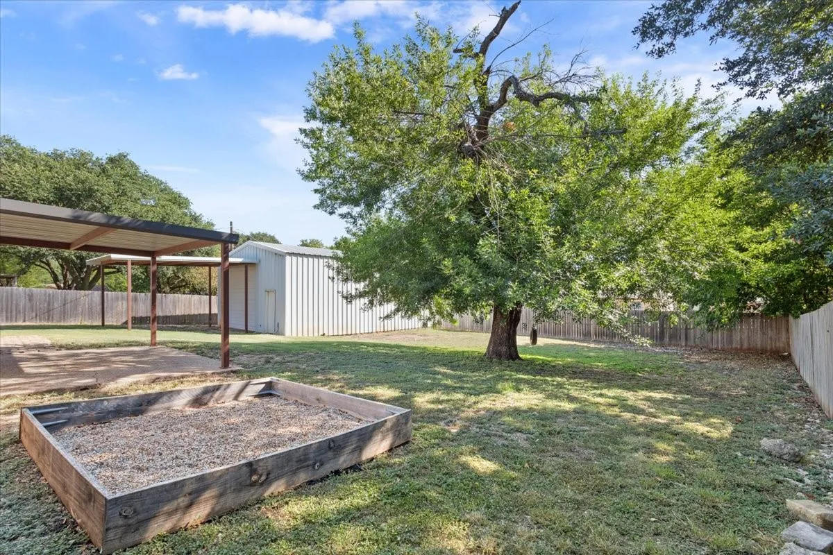 Expansive backyard featuring a large shade tree, a gravel-filled raised garden bed, and a metal storage shed