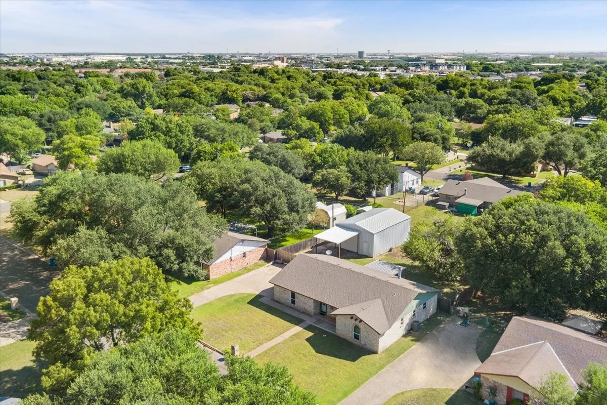 Expansive property featuring a single-story residence with a brown shingle roof, a detached metal building with a carport, and mature trees throughout the grounds