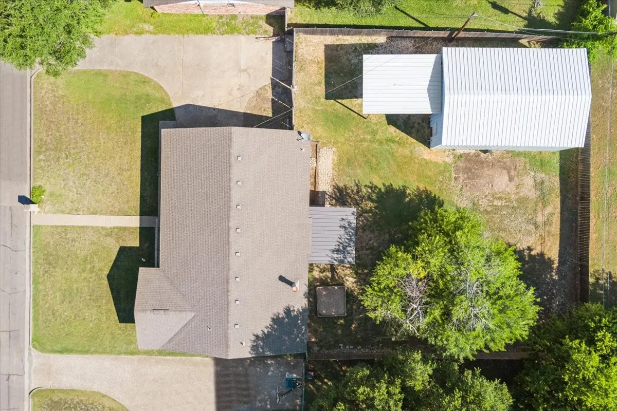 Expansive lot featuring a primary residence with a composite shingle roof, a detached outbuilding with a metal roof, mature trees, a concrete driveway, and a concrete walkway