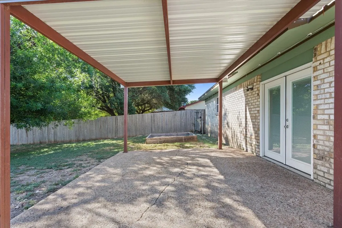 Covered concrete patio with a metal awning, offering direct outdoor access through double French doors
