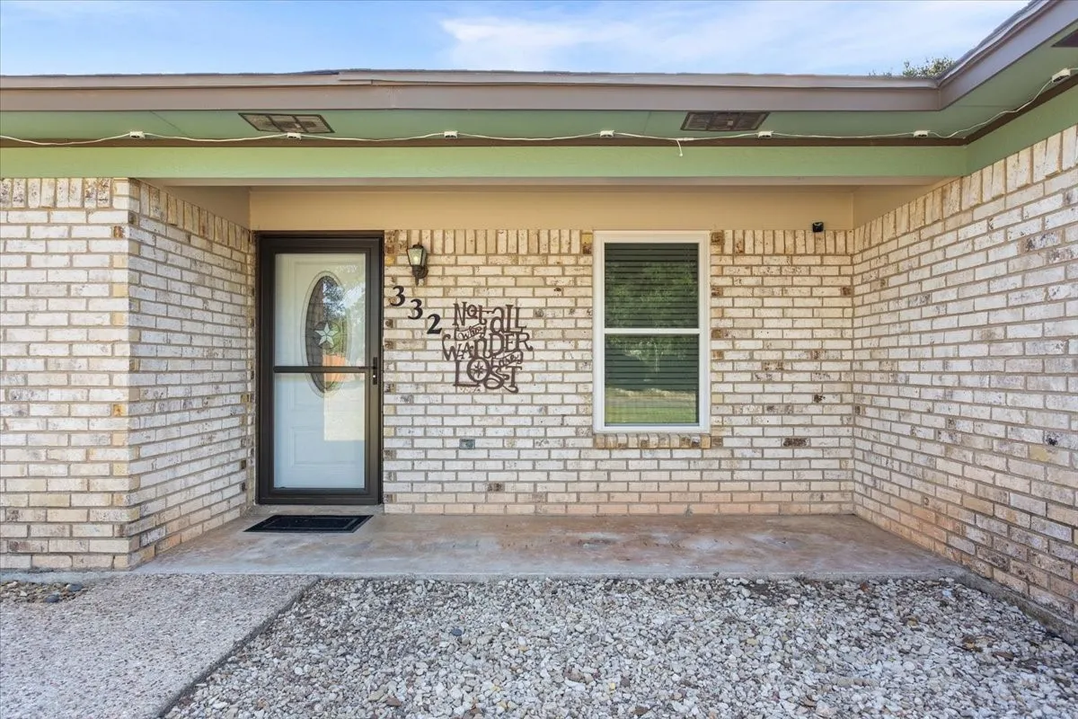 Inviting entry featuring a brick exterior, covered porch, storm door, and an exterior wall light fixture