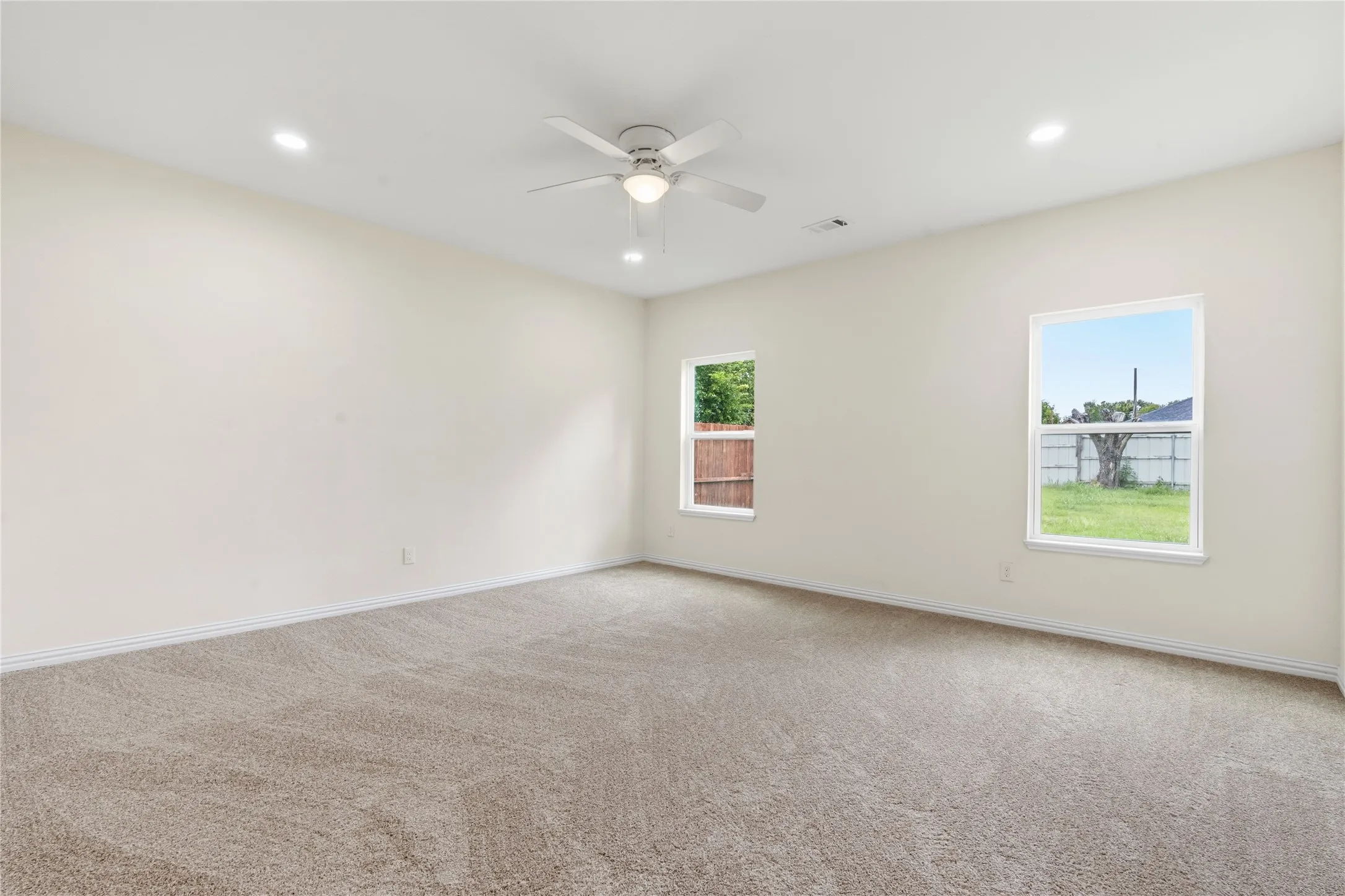 Spacious interior room featuring neutral-toned carpeting, light-colored walls, and two large windows