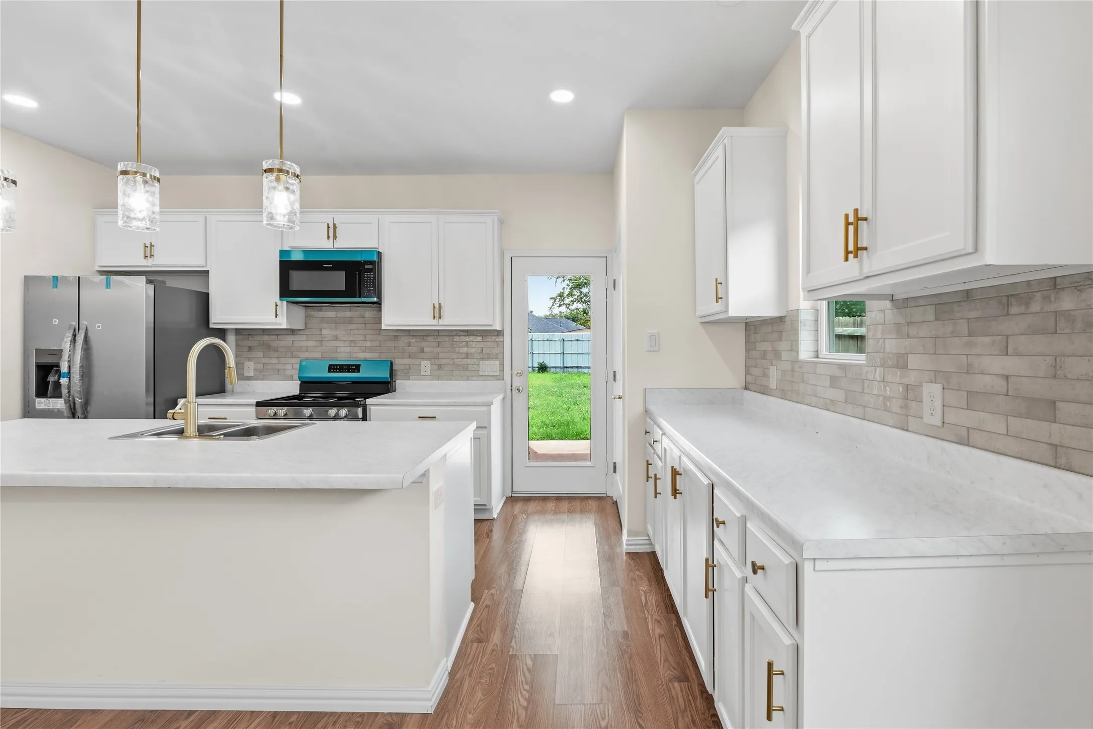 Modern kitchen featuring an island with an integrated sink, white cabinetry with gold-tone hardware, and light-toned countertops