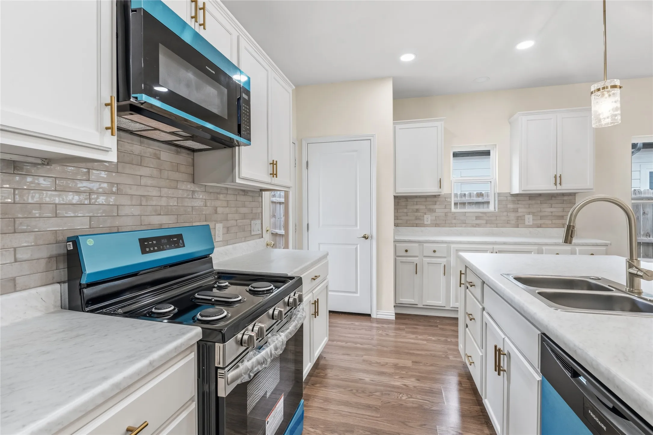Modern kitchen featuring white cabinetry, light-toned countertops, a full subway tile backsplash, and wood-finish flooring