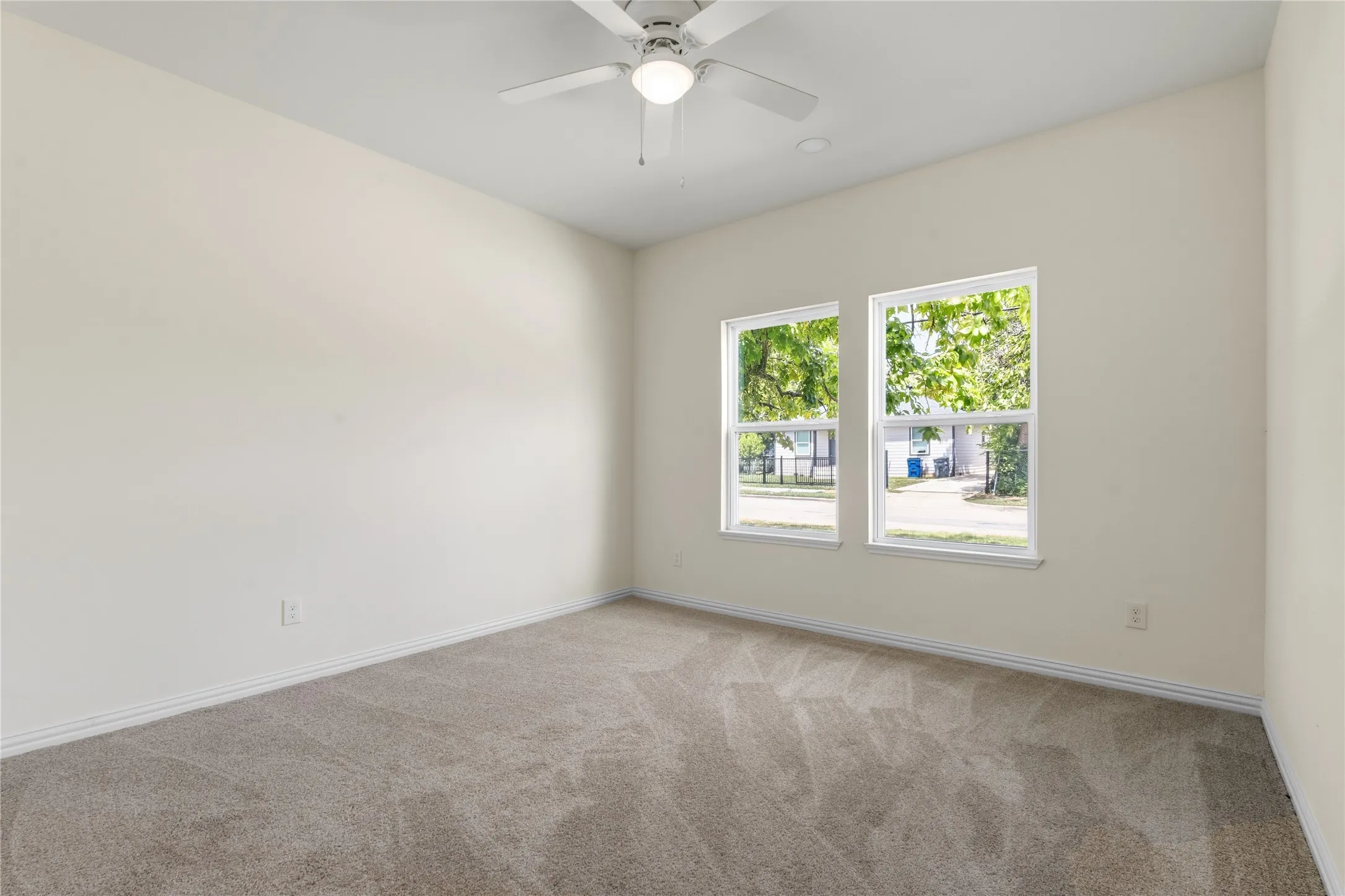 Carpeted interior space featuring dual windows, a ceiling fan with integrated lighting, and white baseboards