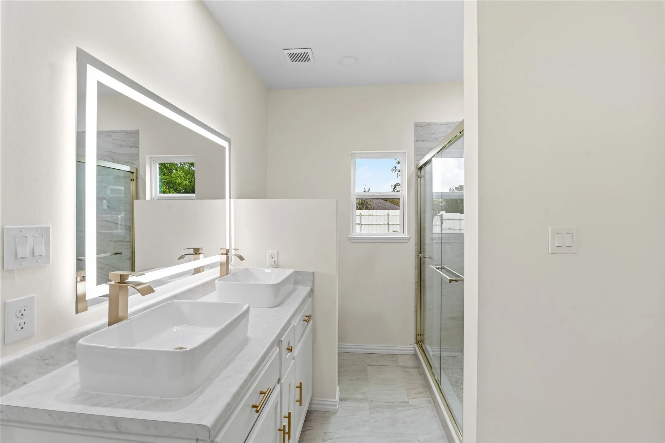 Dual vessel sinks set on a light-toned vanity with golden hardware