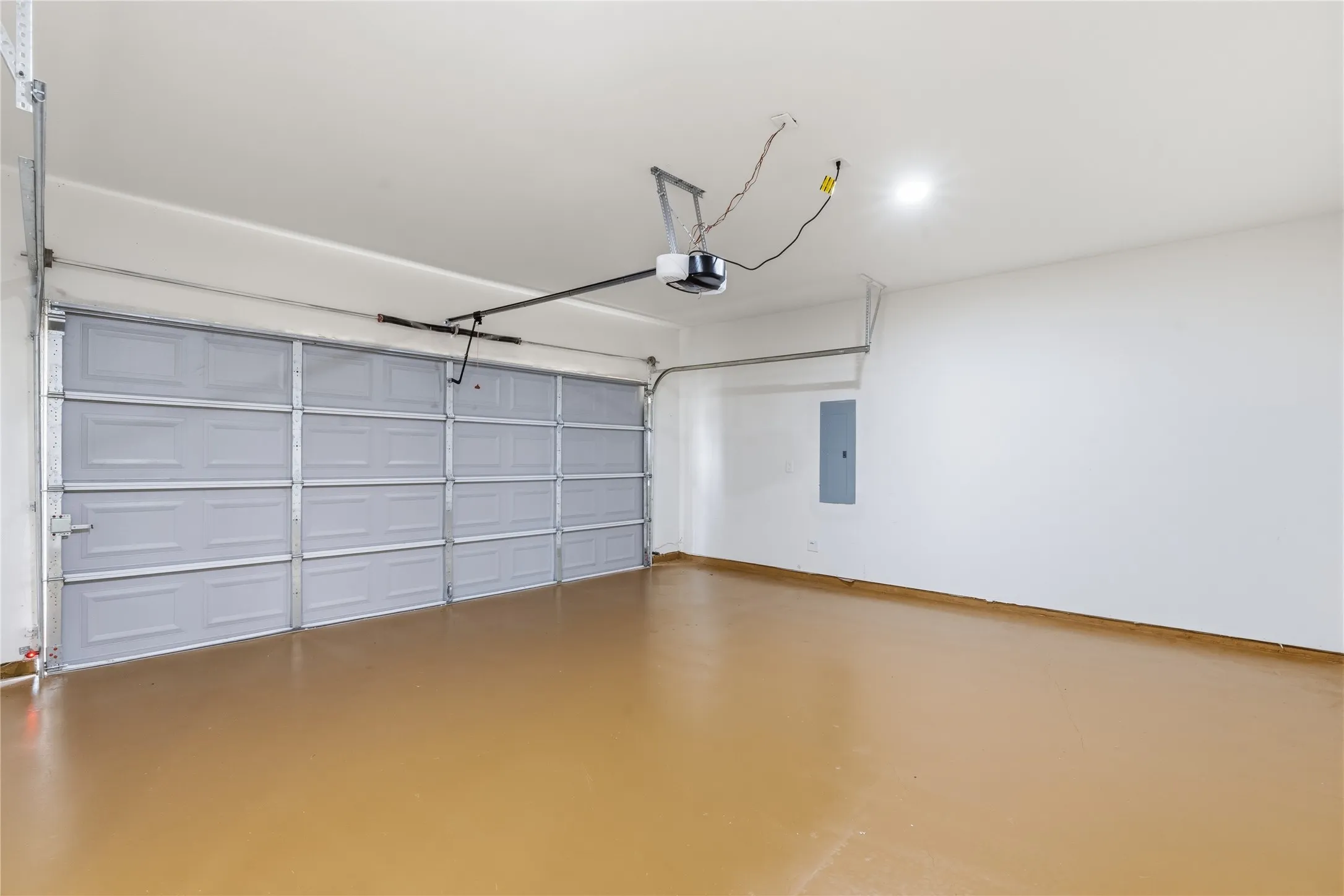 Spacious garage featuring a light gray sectional garage door, an automated garage door opener, an electrical panel, overhead lighting, and a polished concrete floor