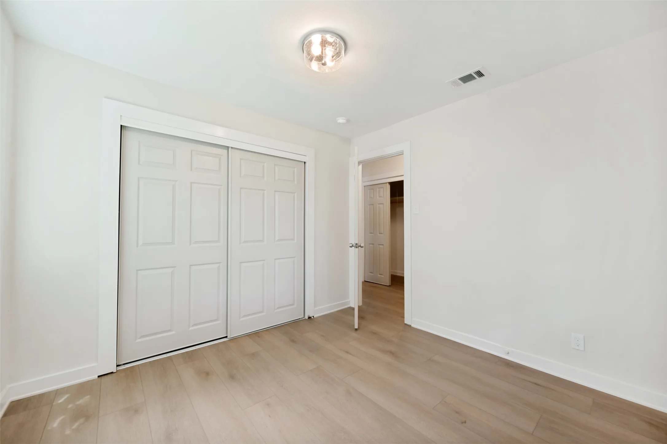 Neutral white wall finishes, wood-finish flooring, and a flush mount light fixture