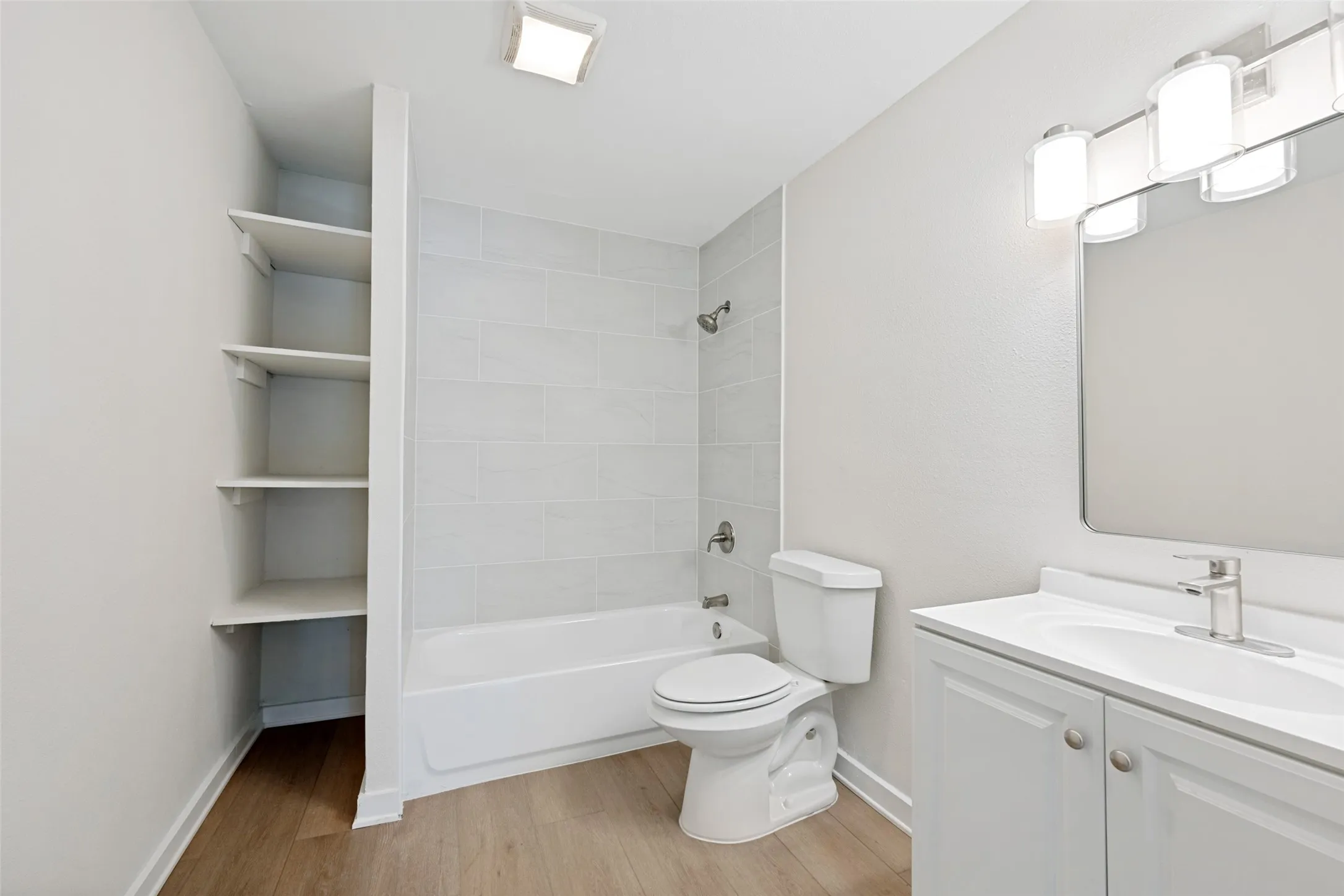 Bathroom featuring a white bathtub, ceramic tiled shower surround, toilet, and built-in shelving