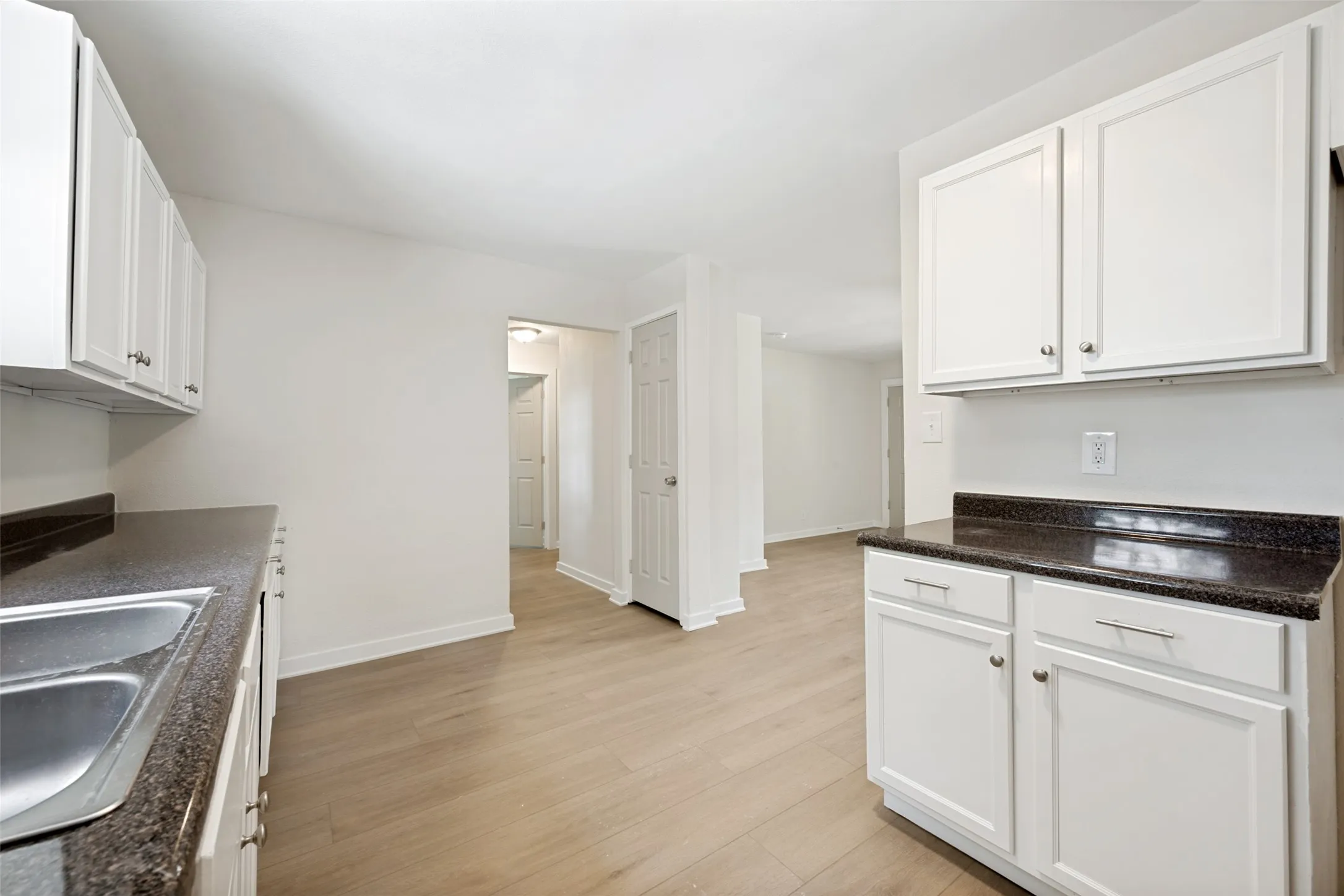 Kitchen featuring wood-finish flooring, white cabinetry, dark speckled countertops, and a double basin stainless steel sink
